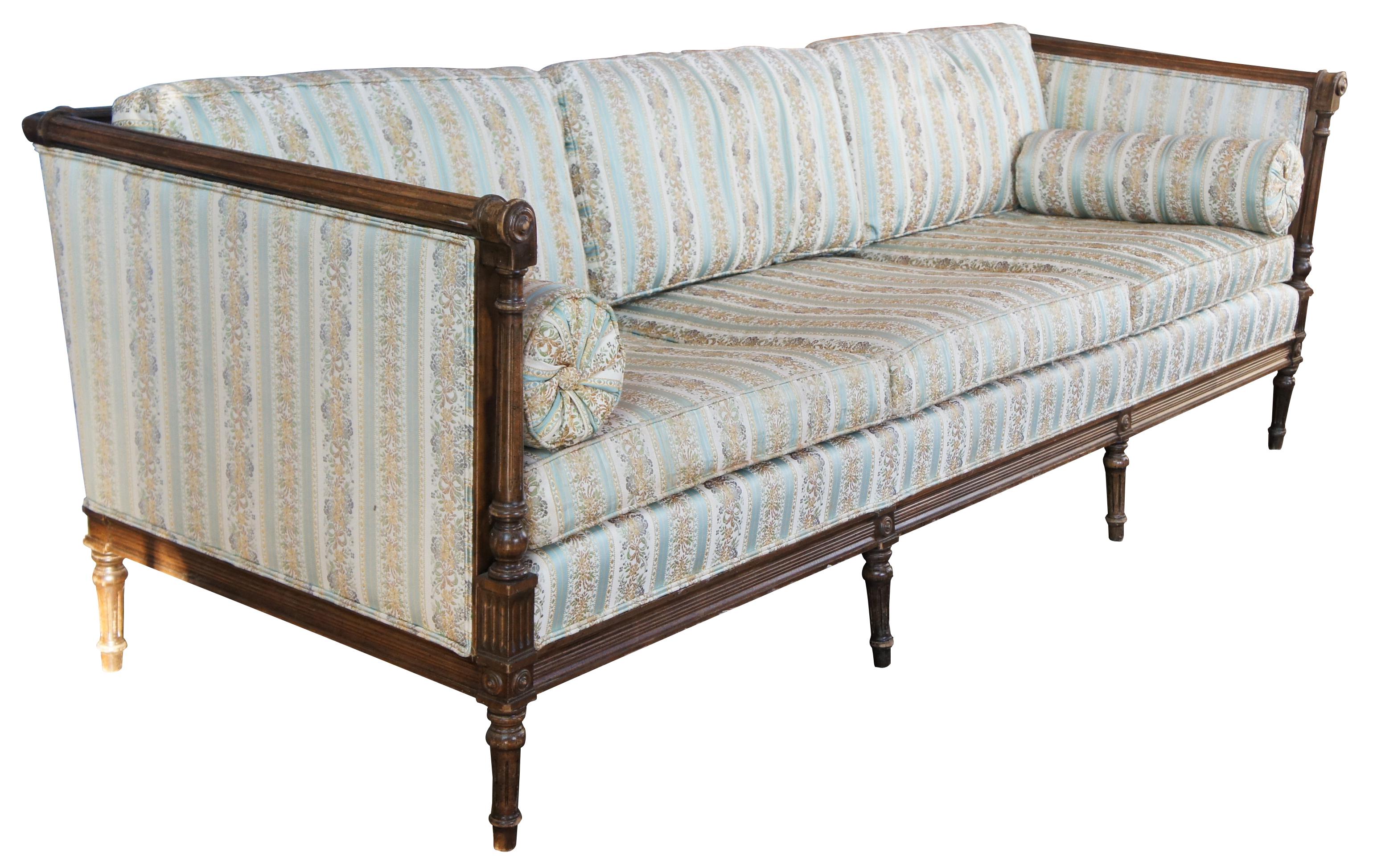 Antique Louis XVI style three seat upholstered sofa or couch. Features a naturally distressed and carved walnut frame with fluted tured columns, eight legs and silk upholstery with bolster pillows. Measures: 87