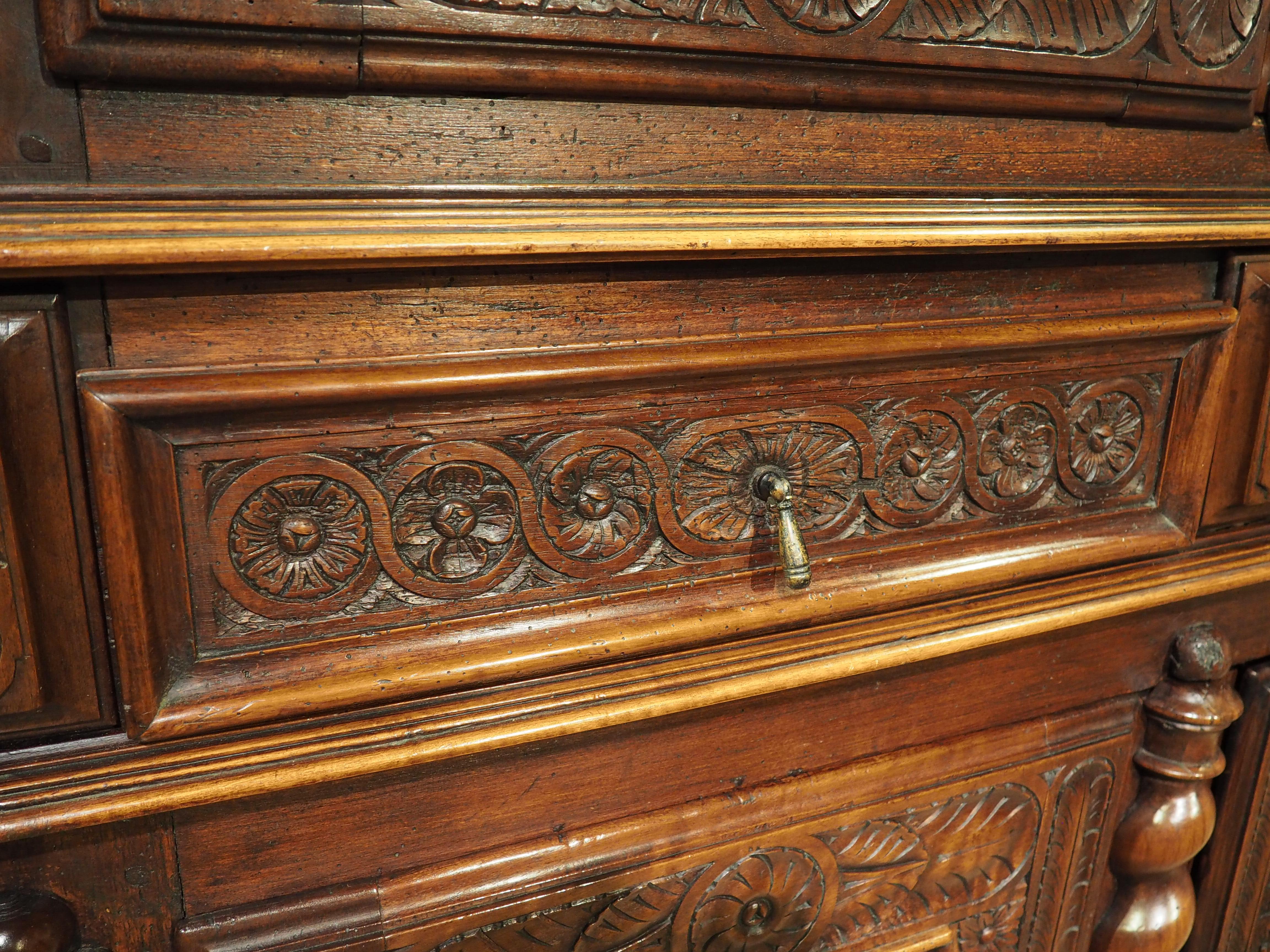 Hand-carved from walnut wood and embellished with gilt highlights, this stunning four door buffet deux corps was produced around Lyon, France, during the mid to late 1600’s. The two-bodied storage piece, which has large bun feet in the front, can be