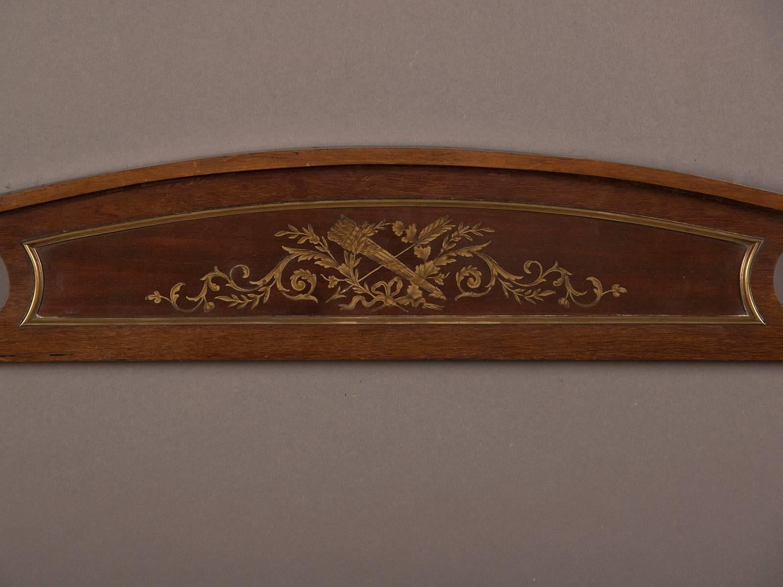 An antique French Louis XVI architectural fragment from a bibliothèque made of mahogany inlaid with brass from France circa 1870. The simple arch top frames the Louis XVI pattern of a quiver of arrows amidst a group of twining foliage. This piece