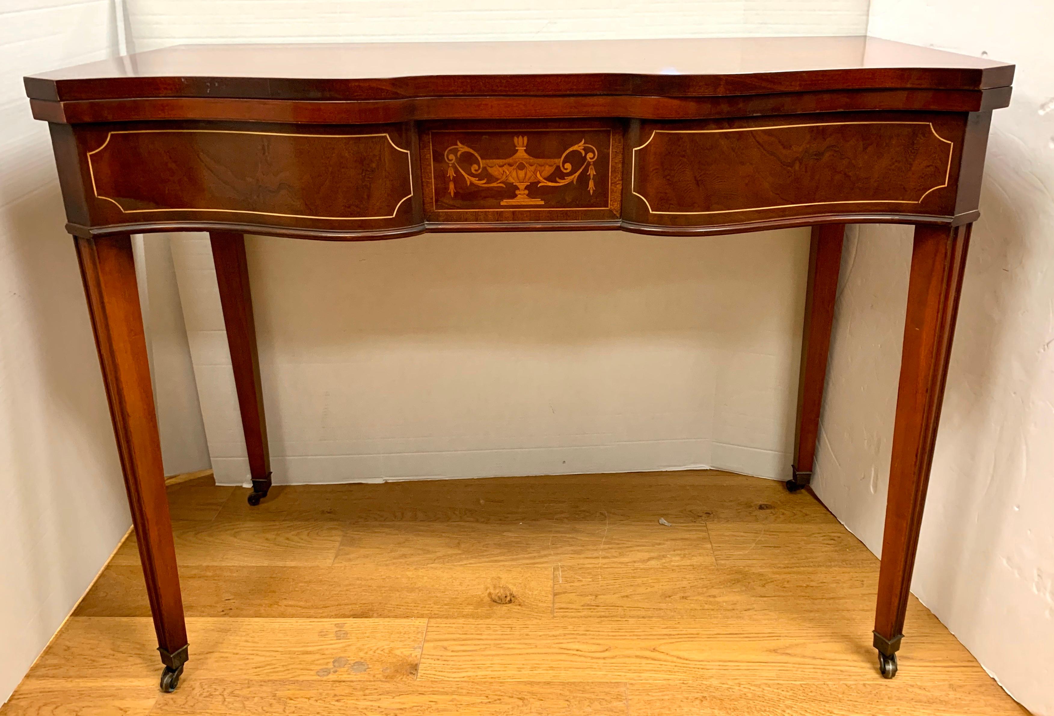 Elegant mahogany game table with gorgeous urn and line inlay on its shaped front. 
Extraordinary craftsmanship, circa 1920s, France. Table flips open to expand to a square game table or breakfast table. The table rests on tapered legs with brass