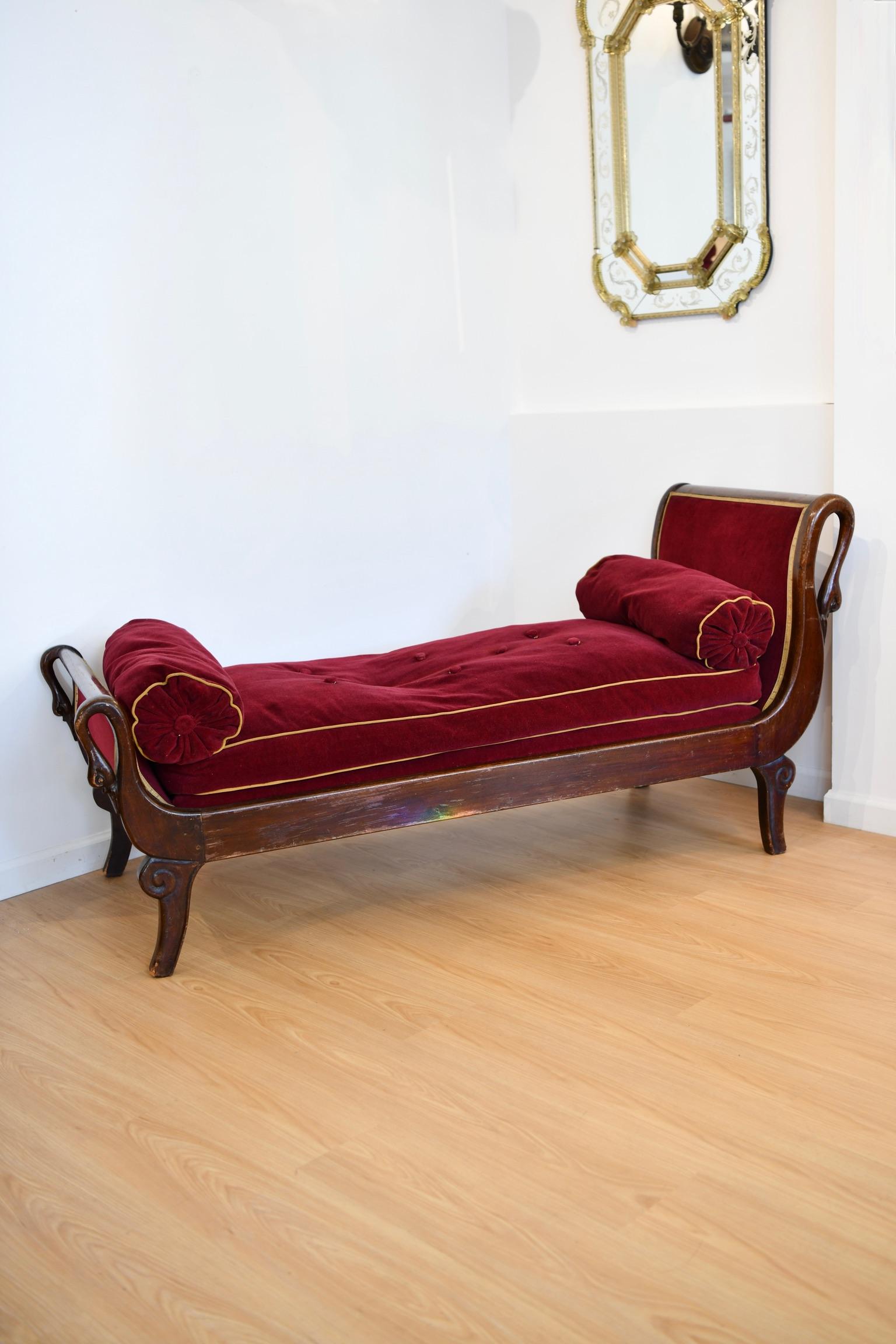 Antique French mahogany chaise lounge with carved swan heads at posts, maroon upholstery and bolster pillows, circa 1930. Matching chairs available, sold separately. Dimensions: 32.5