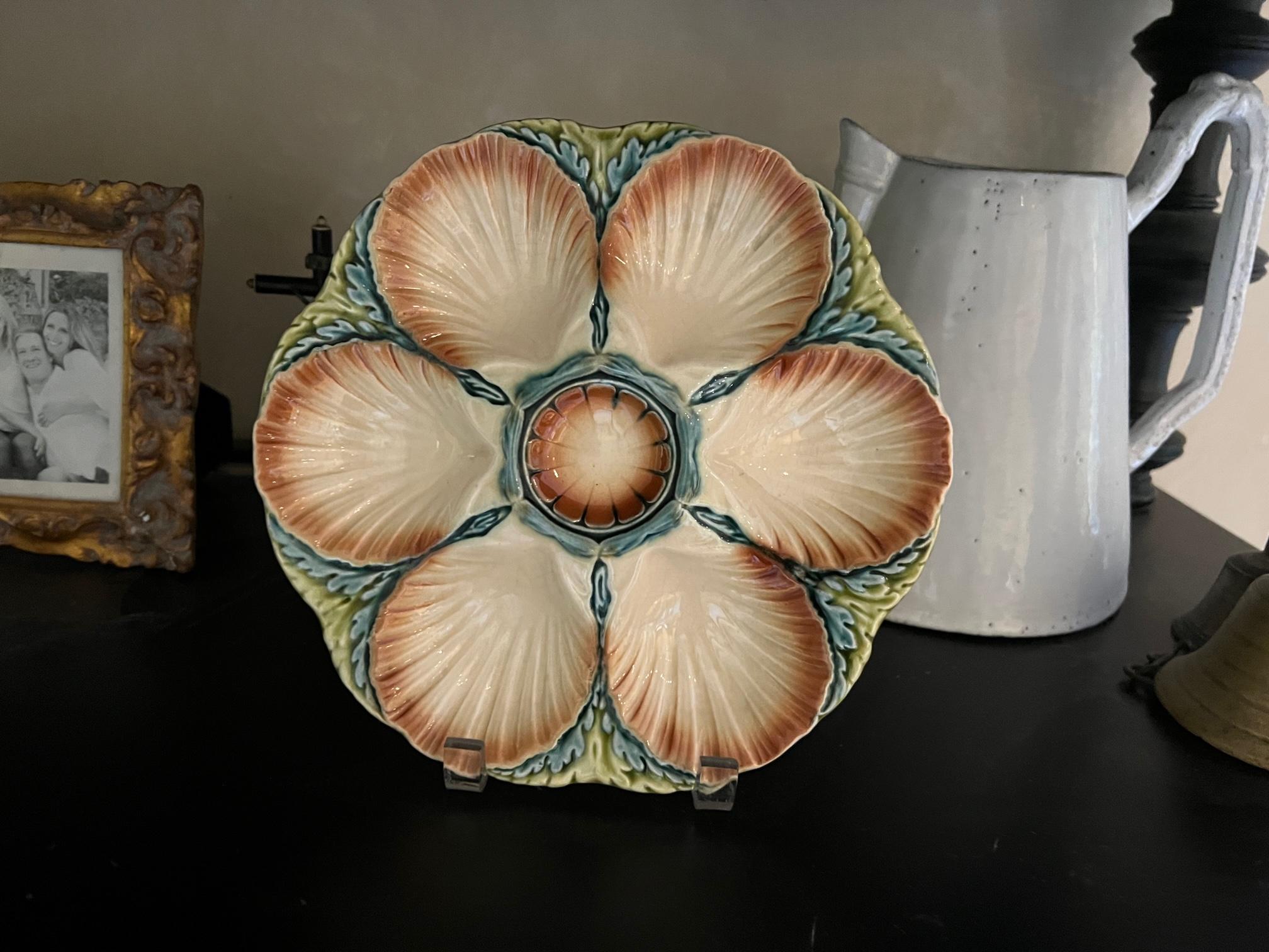Antique French majolica oyster plate made by Sarreguemines around 1890. The plate has a seaweed motif on the edges with six shell shaped wells for oysters or scallops. The center well is for lemon or sauce.