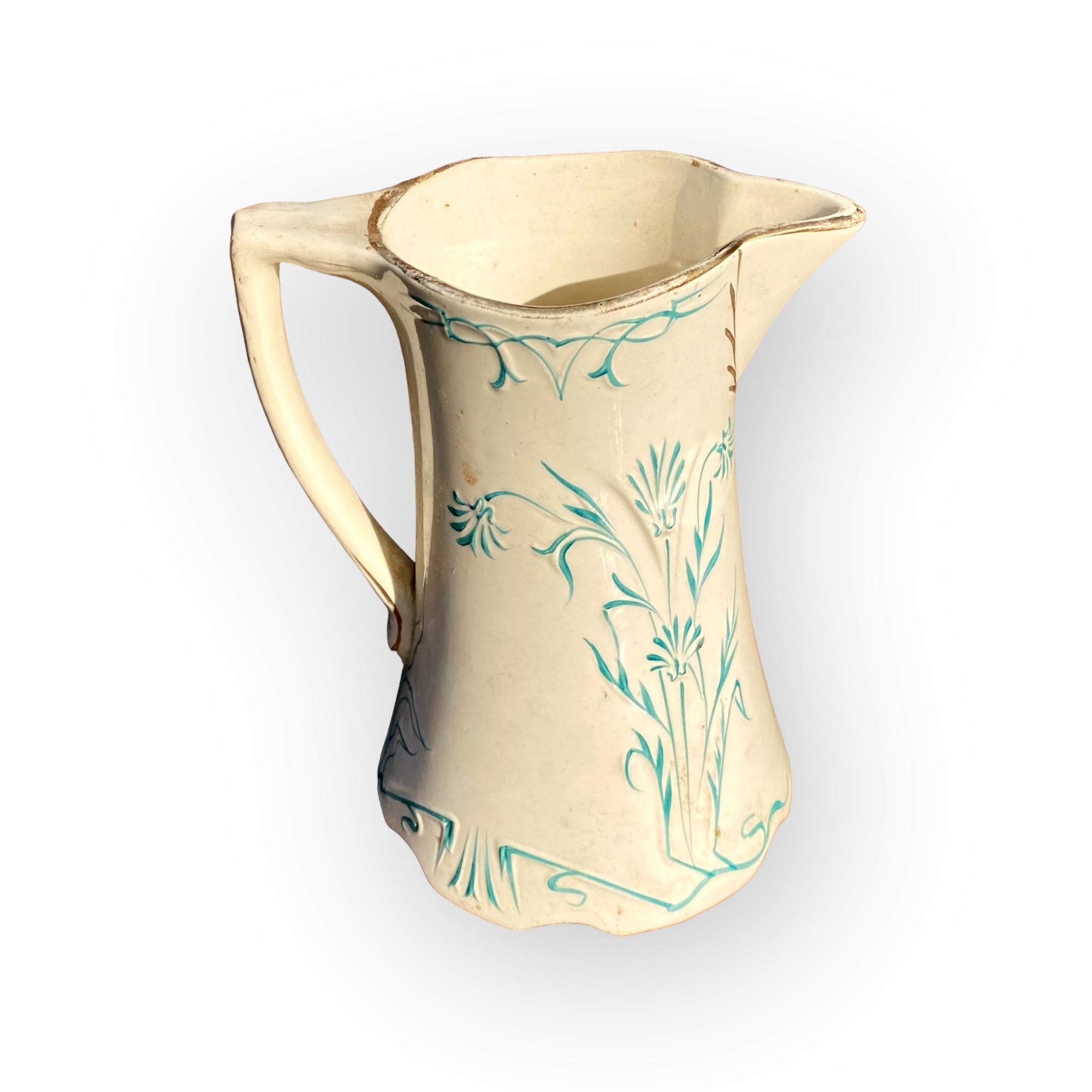 Splendida brocca in maiolica francese di St. Amand & Hamage Nord, di gusto nouveau, della fine del XIX secolo, con suggestivi disegni di fiori e fogliame in tonalità verde acqua, evidenziati da bande dorate e manico a lobi sulla base