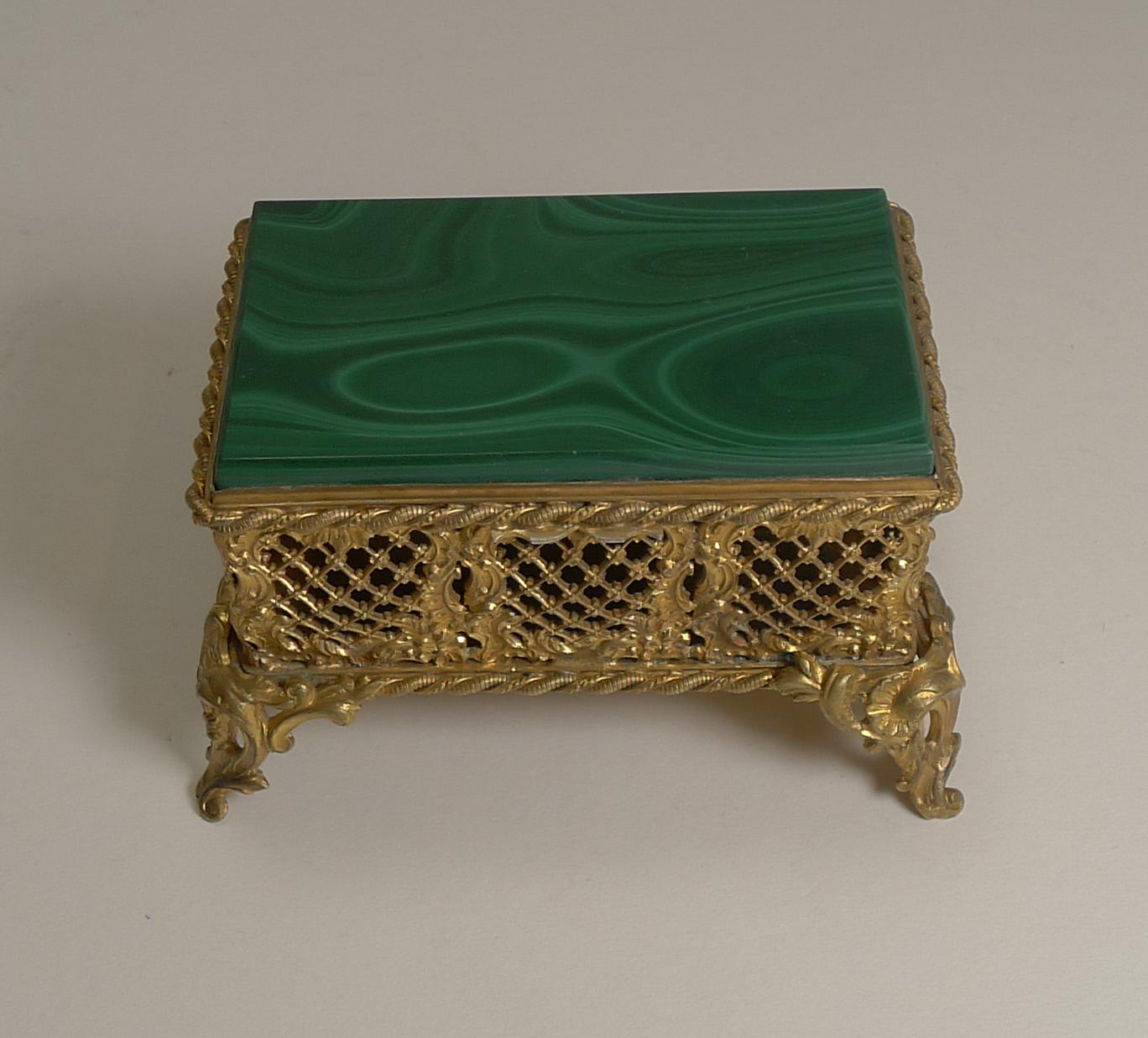 A stunning late 19th century box made from gilded brass or bronze, on four highly decorative legs and the sides intricately pierced of reticulated panels.

The top is inset with a perfectly preserved tablet of Russian Malachite without damage and