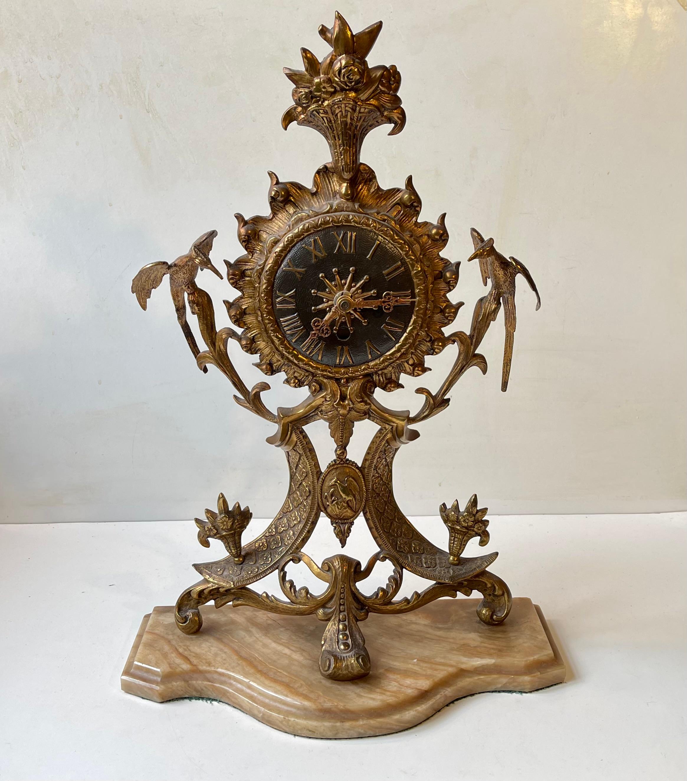 Ornate mantel clock in ormolu gilt brass upon a marble base. Extensive details: guarding eagles, center code of arms, Roman numerals, partially pierced and engraved hands upon a star or sun center-disc, floral ornament etc. Its European and was