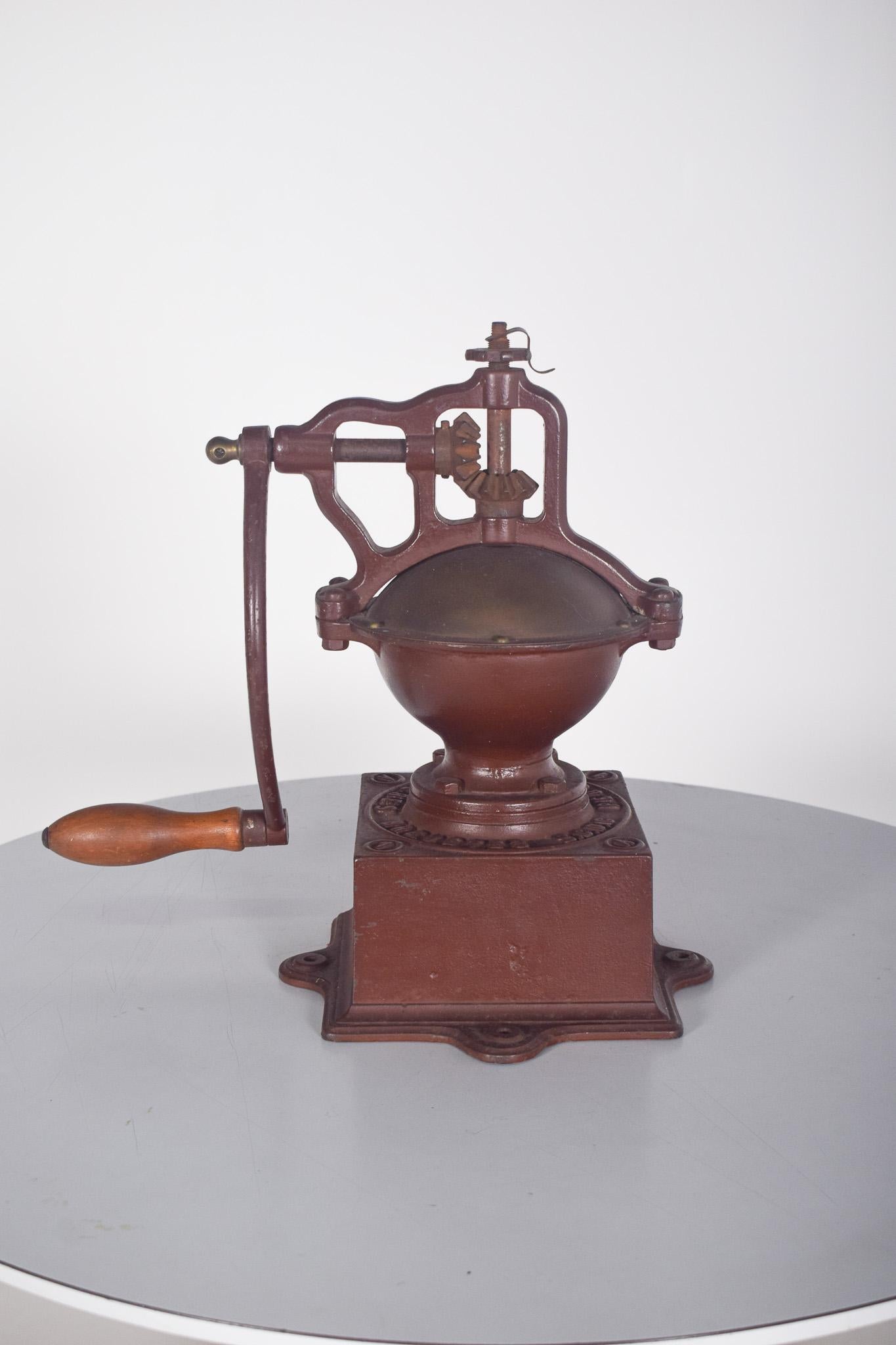 Macinacaffè manuale. Con una struttura robusta, ha un design classico che si distingue per la cupola metallica arrotondata e la base rettangolare con iscrizione in rilievo. La lunga manovella, con un manico in legno tornito, consente un utilizzo