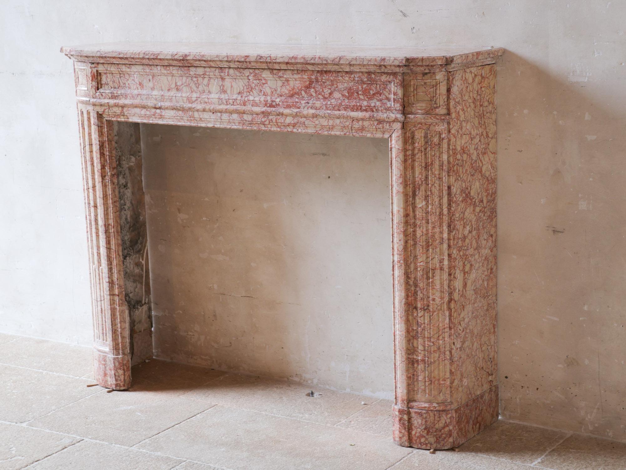Antique French marble fireplace in pink tones. A 19th century Demi Lune Louis XVI mantelpiece in Trets marble, with fluted jambs and frieze panels.

Dimensions: h 106 x w 136 x d 35 cm
Inner dimensions: h 85 x w 90 cm
