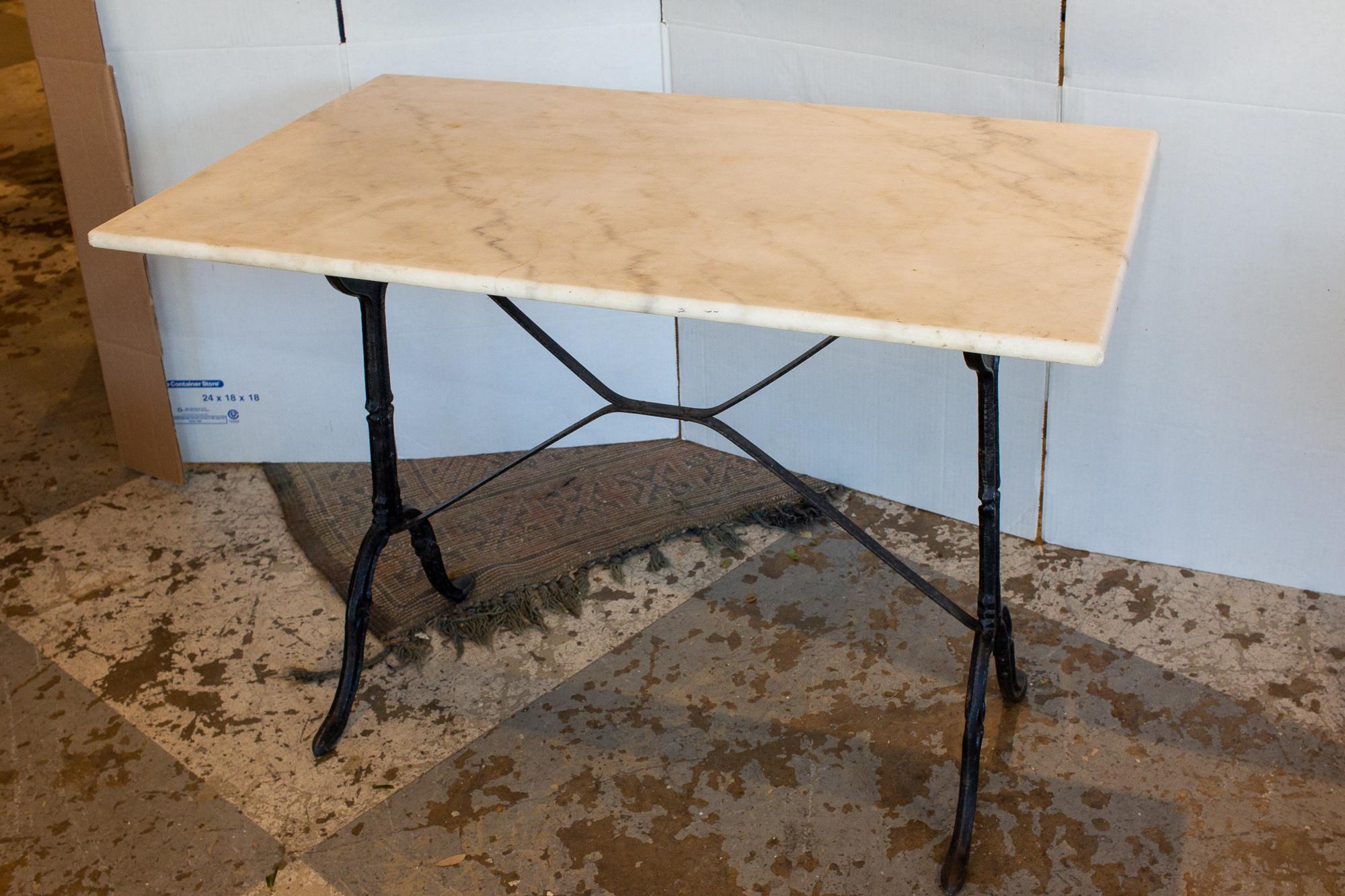 This antique French bistro table features a white marble top and a black iron base. The top is finished with a Demi-bullnose edge. The marble has some grey veining present and some very light discoloration. The base is black and does have some wear,