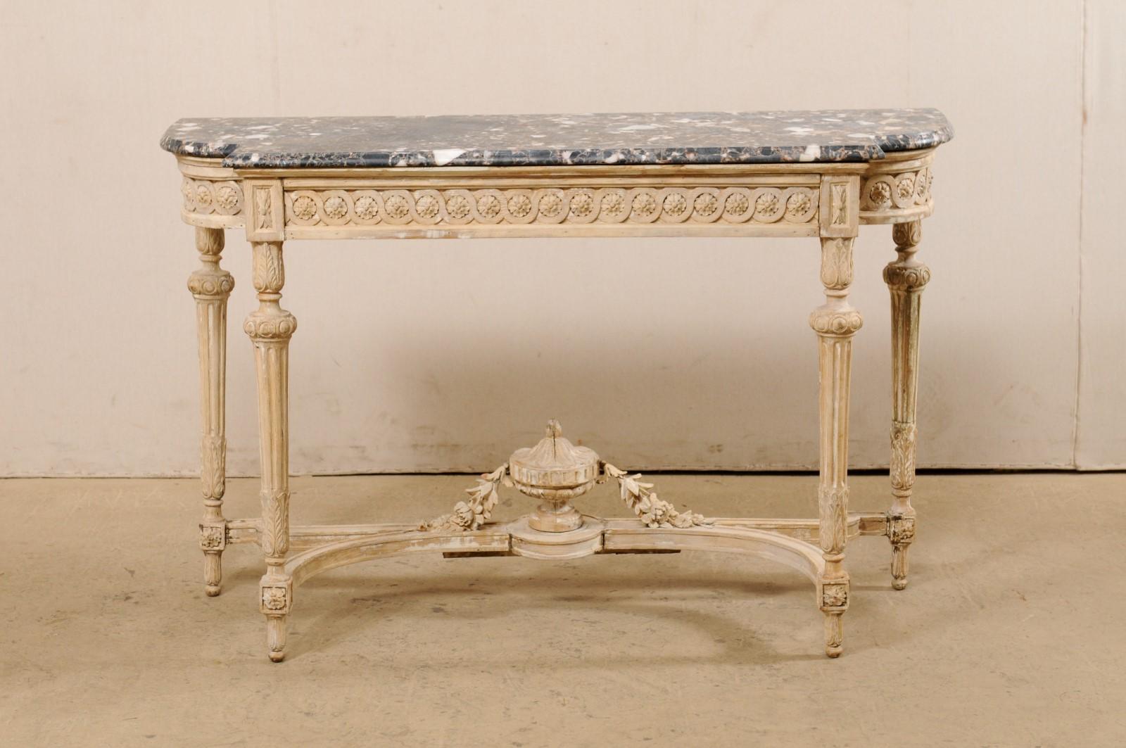 A French marble-top console table, with carved urn finial accent at underside, from the 19th century. This antique table from France features an oblong shaped top with flattened backside and curved and stepped out shaped front. The marble top is
