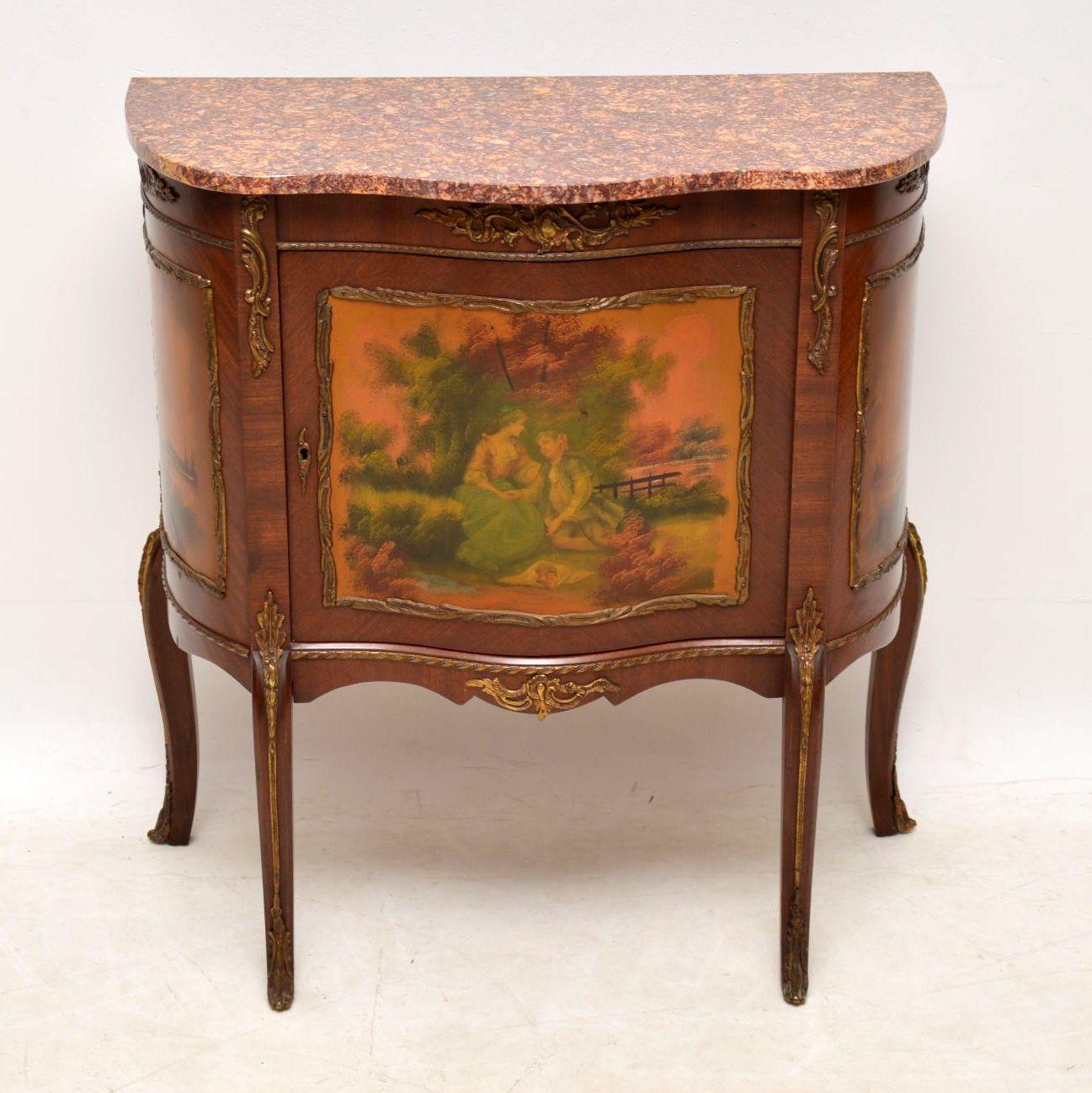 Antique French marble top side cabinet with decorative scenes on the door and side panels. It’s in good original condition & dates from around the 1930s period. The marble is really nice & there are lots of gilt mounts all over this cabinet. The