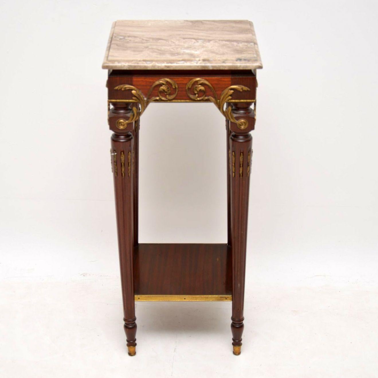 This antique French marble top mahogany side table could be used as a stand to display something on. It has the original marble top, turned fluted legs, a bottom platform and sits on gilt metal feet. This table has gilt bronze mounts all around the