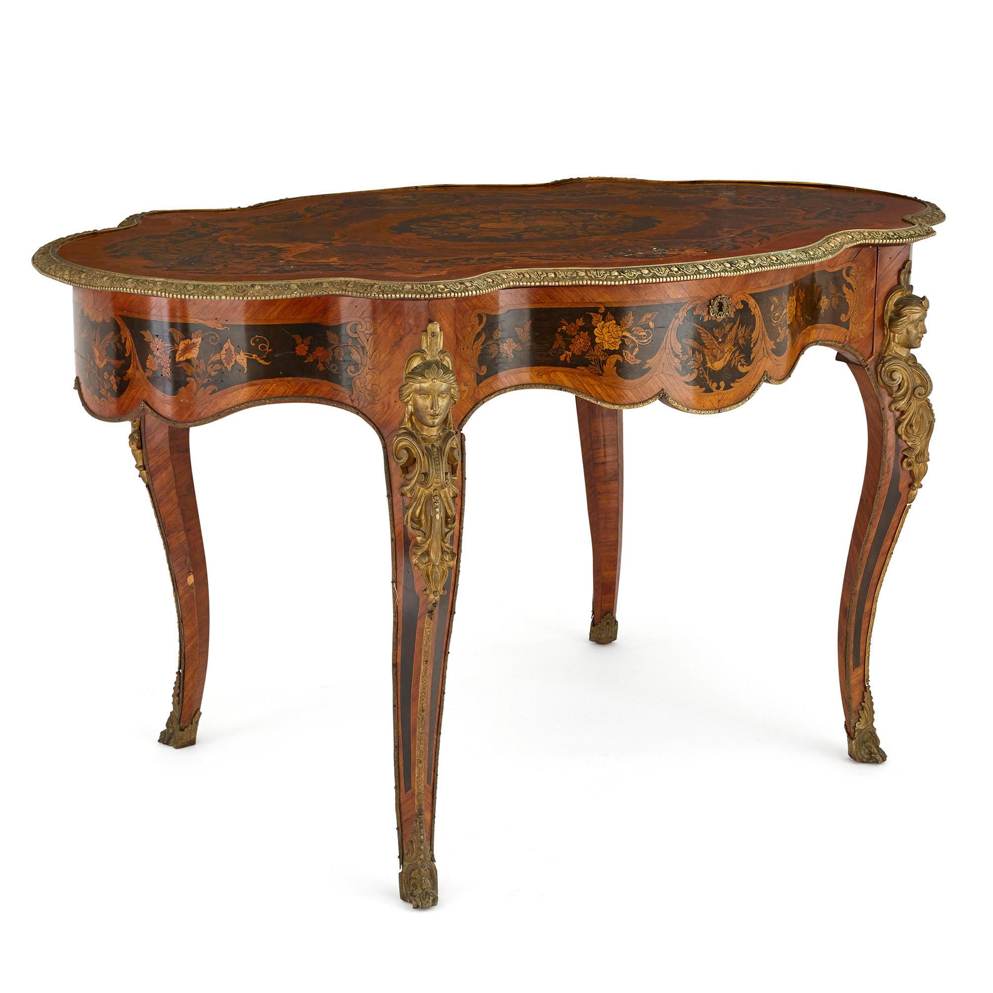 This table is an exquisite piece of French antique furniture. The table is covered with beautiful marquetry work and finely-cast gilt bronze (ormolu) mounts. 

The table features a shaped oval top which is decorated with bands of pattern, created