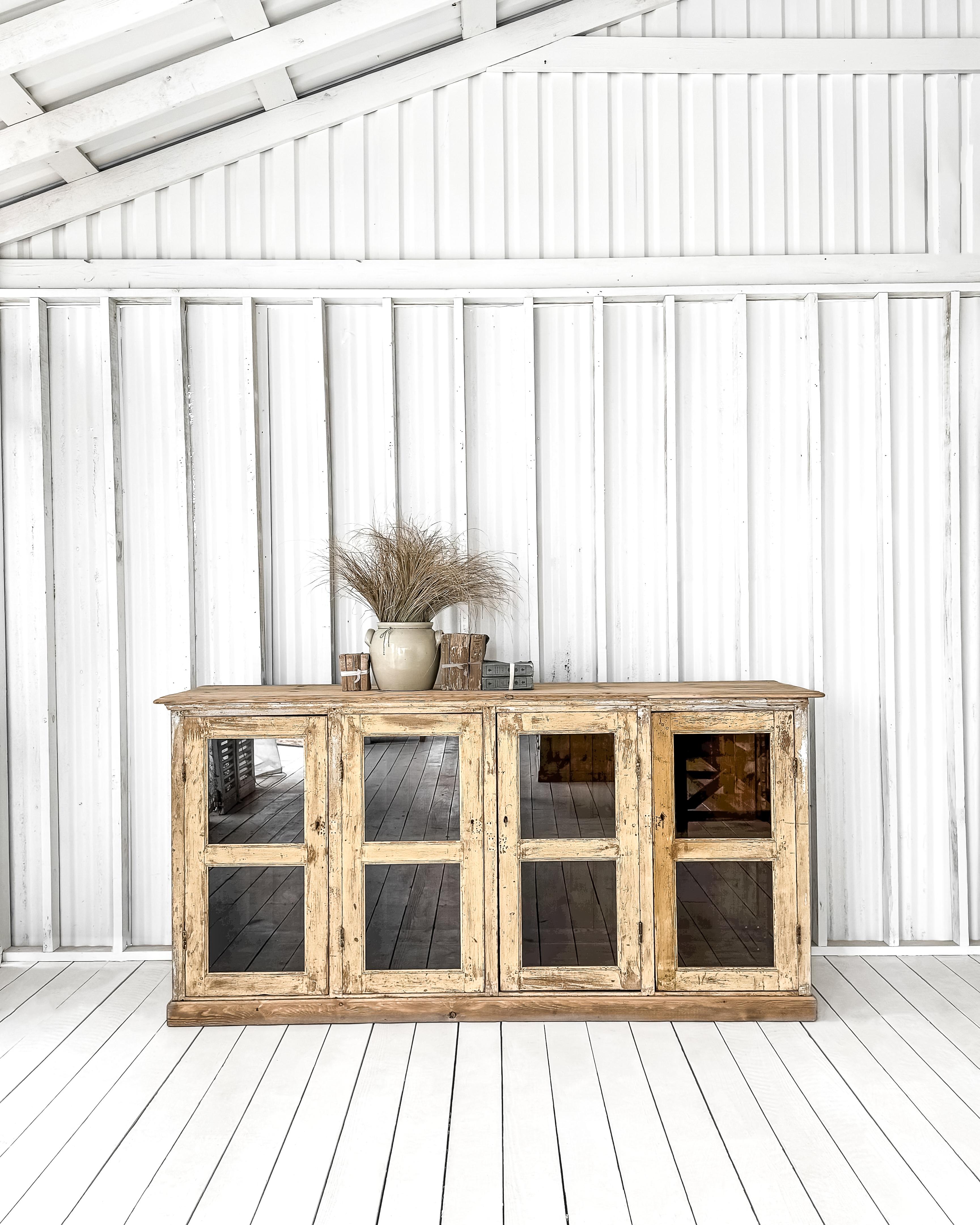 A large and handsome solid wood mercantile display cabinet found in France. This beauty boasts four framed glass doors, making it perfect for showcasing your collectibles.

Crafted with raised paneled sides, an ogee edge top, and a thick baseboard,