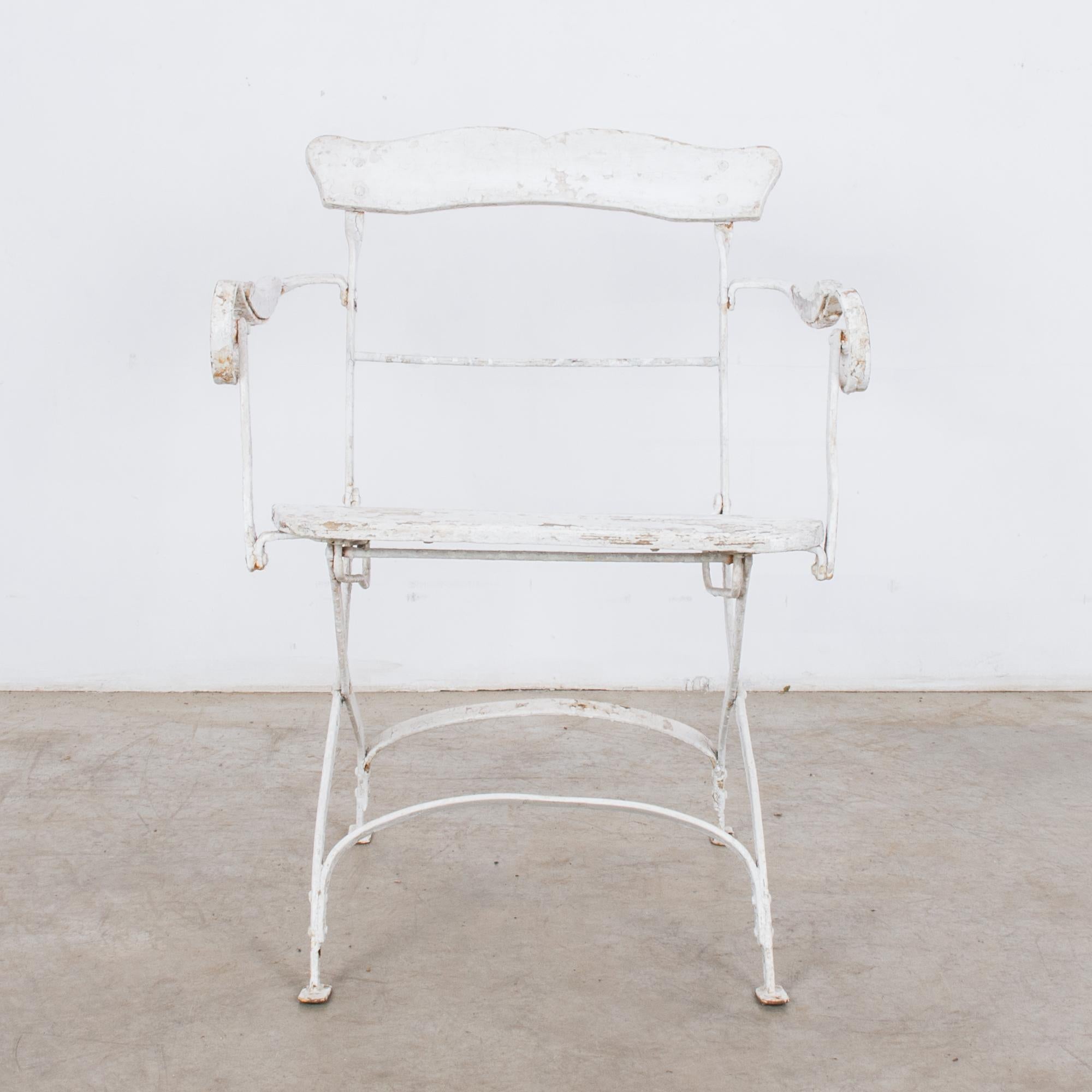 This metal garden chair was made in France. Originally painted white, the chair features a lovely patina, which evokes the rustic ambience of the French countryside. The scroll armrests and curves of the back and legs give the chair a graceful