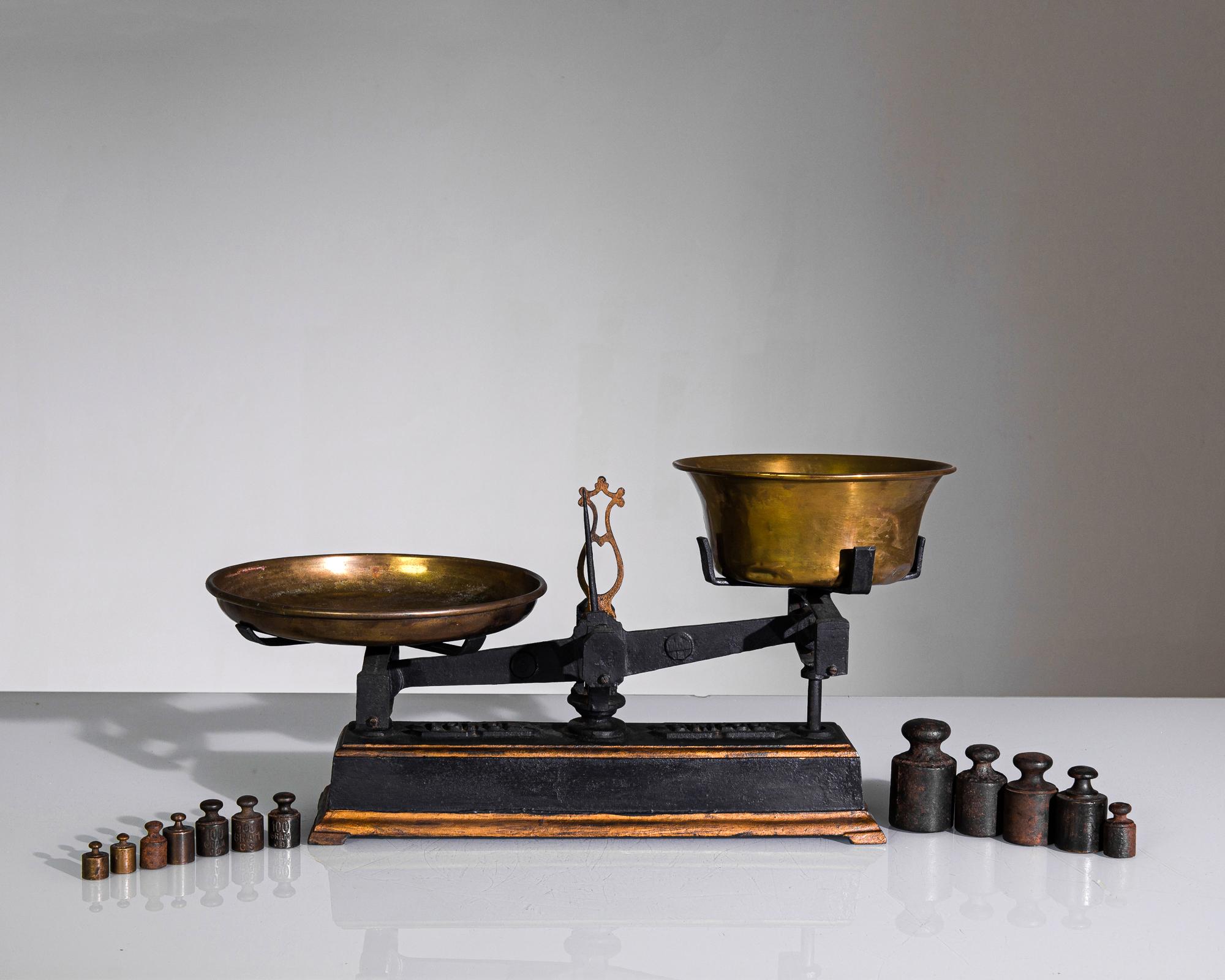 This antique collection of scales and weights was made in France. Scales of these dimensions were commonly used to weigh fruits and vegetables. The burnished brass plates are set on a cast iron base with a complementary black and amber finish.