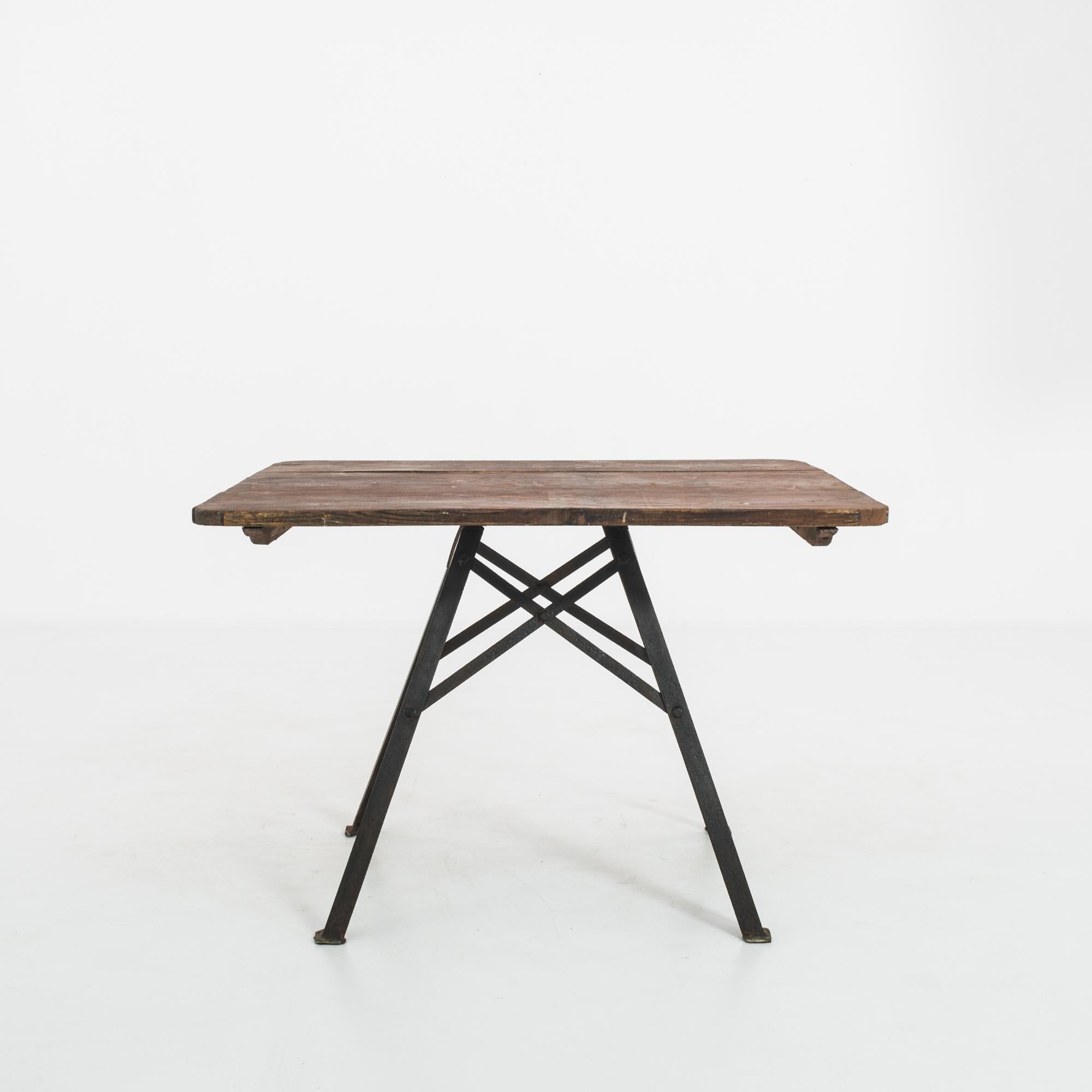 This metal table with a wooden top was made in France and offers an industrial edge with a rustic touch. Planks of wood with a patinated chocolate brown finish comprise the tabletop. Four splayed legs and X-shaped stretchers converge to lend a