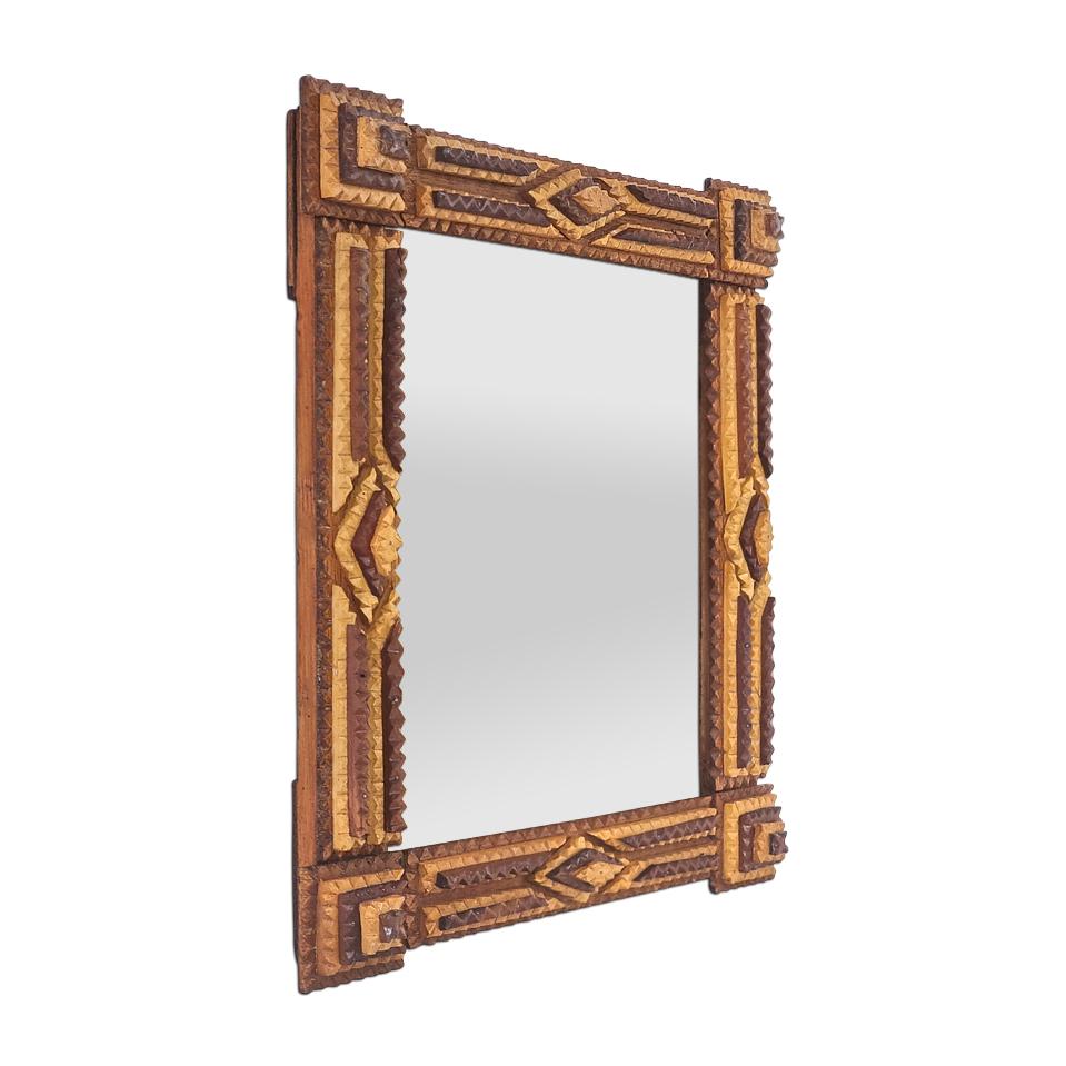 Antique French mirror in two-tone carved varnished wood, circa 1920. In the “Tramp Art” style with geometric carved decorations, square shapes, and oriental-inspired diamonds. Frame width: 4.5 cm / 1.77 in. Modern glass mirror. Antique Wooden rear