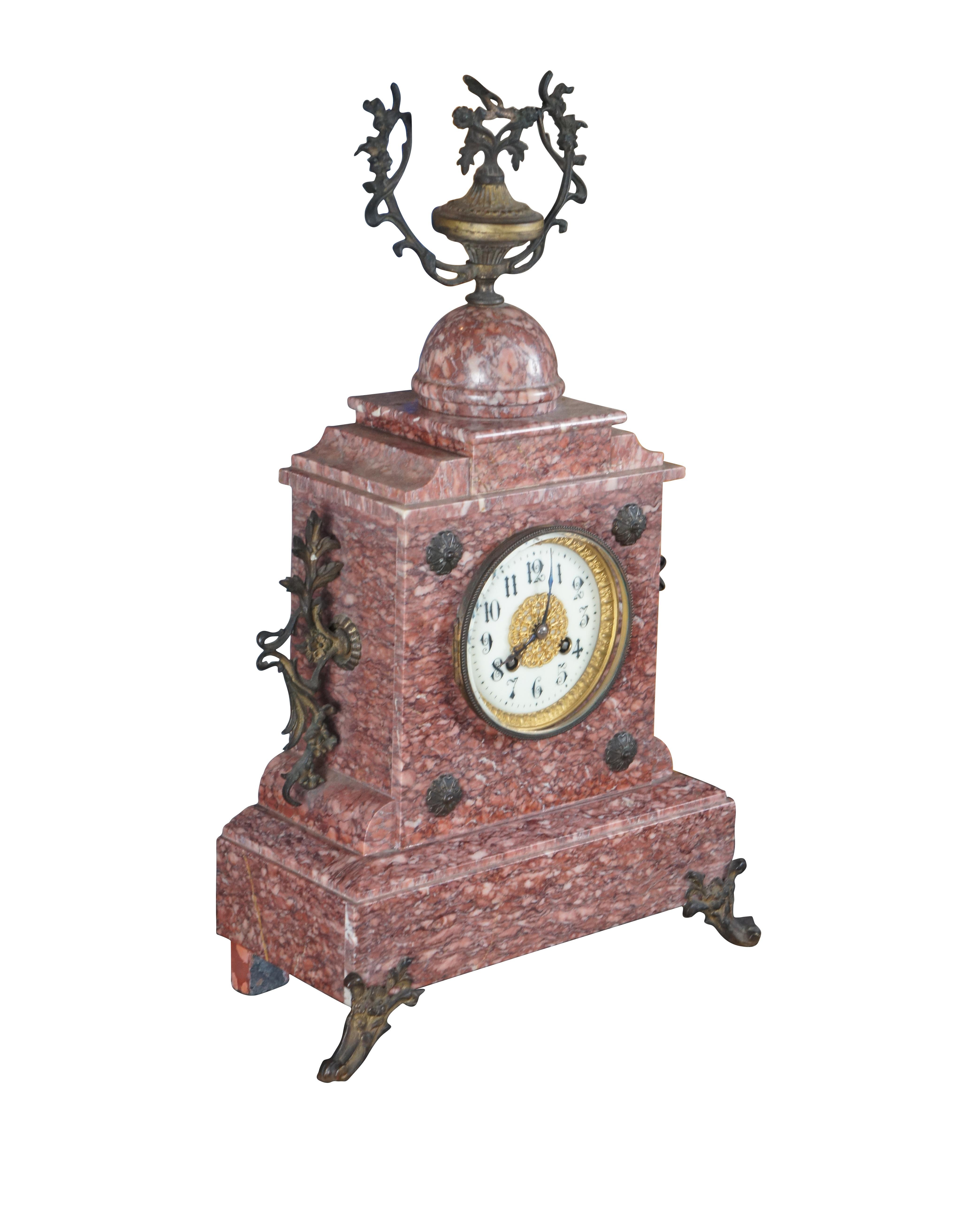 An antique 19th Century mantel Clock. Made from Rouge marble with bronze ormolu. Ornately designed with gold filigree face, a stepped base, footed over downswept legs. Features ornate medallions along the front and bronze motifs.

Dimensions:
12.5