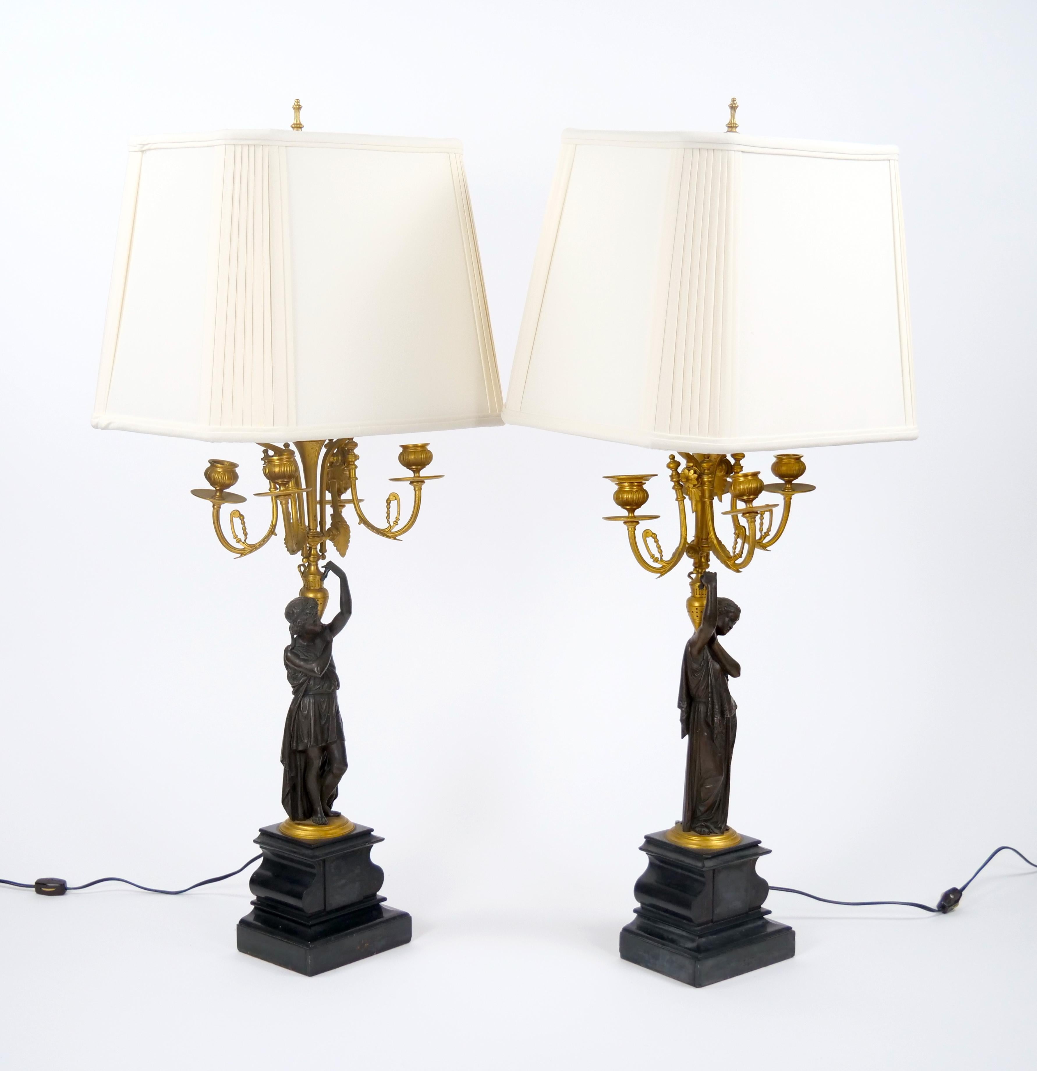 These stunning 19th-century French Napoleon III-style gilt bronze candelabra table lamps capture the opulence and artistry of the period. Each lamp showcases a finely sculpted figure of a woman in classical attire, gracefully holding a torch-shaped