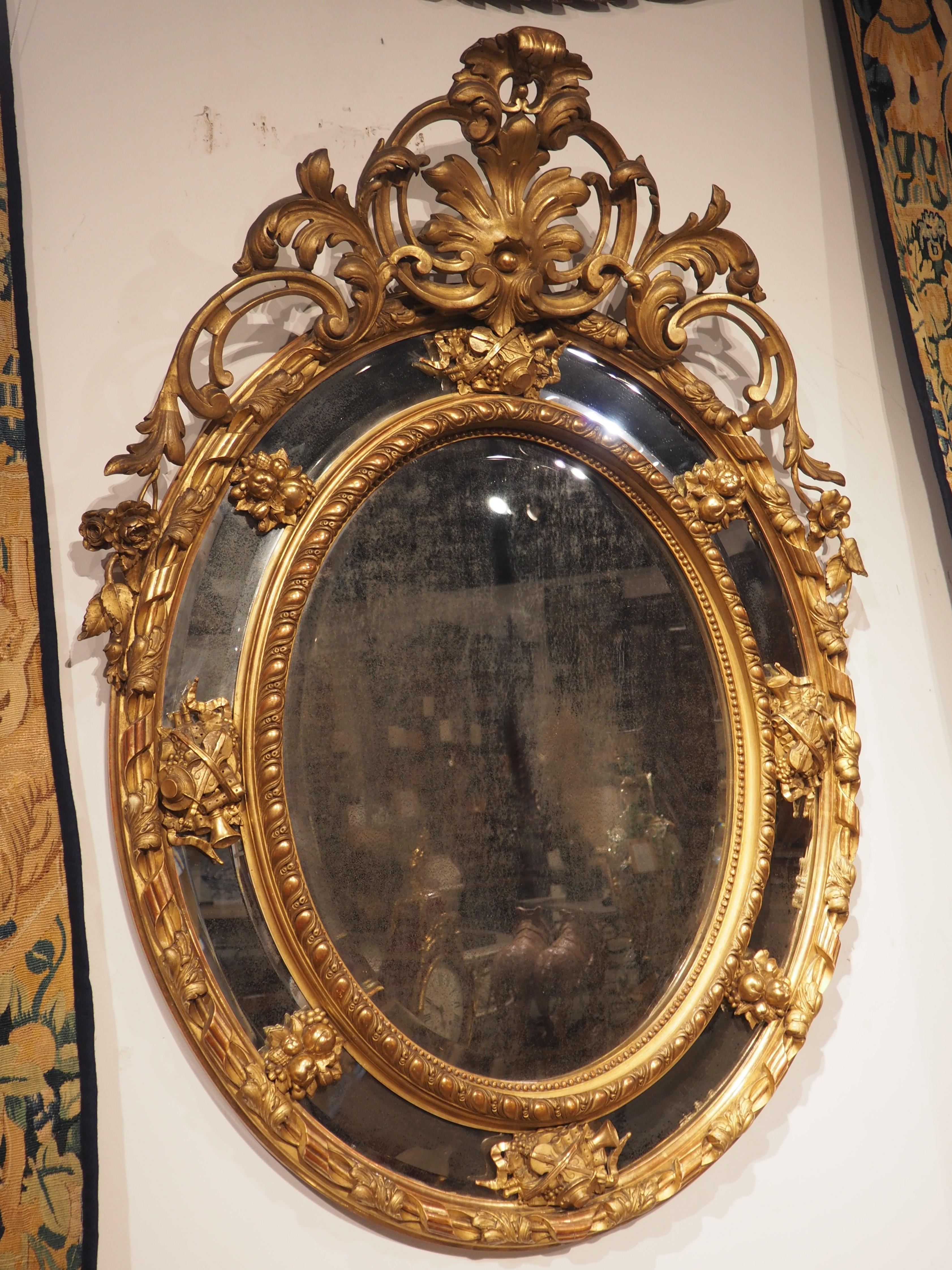 Known as a miroir à parcloses, this oval giltwood mirror with musical trophy décor was hand-carved in France, circa 1860. The mirror dates to the reign of Napoleon III (sometimes referred to as Second Empire), a time when decorative elements were