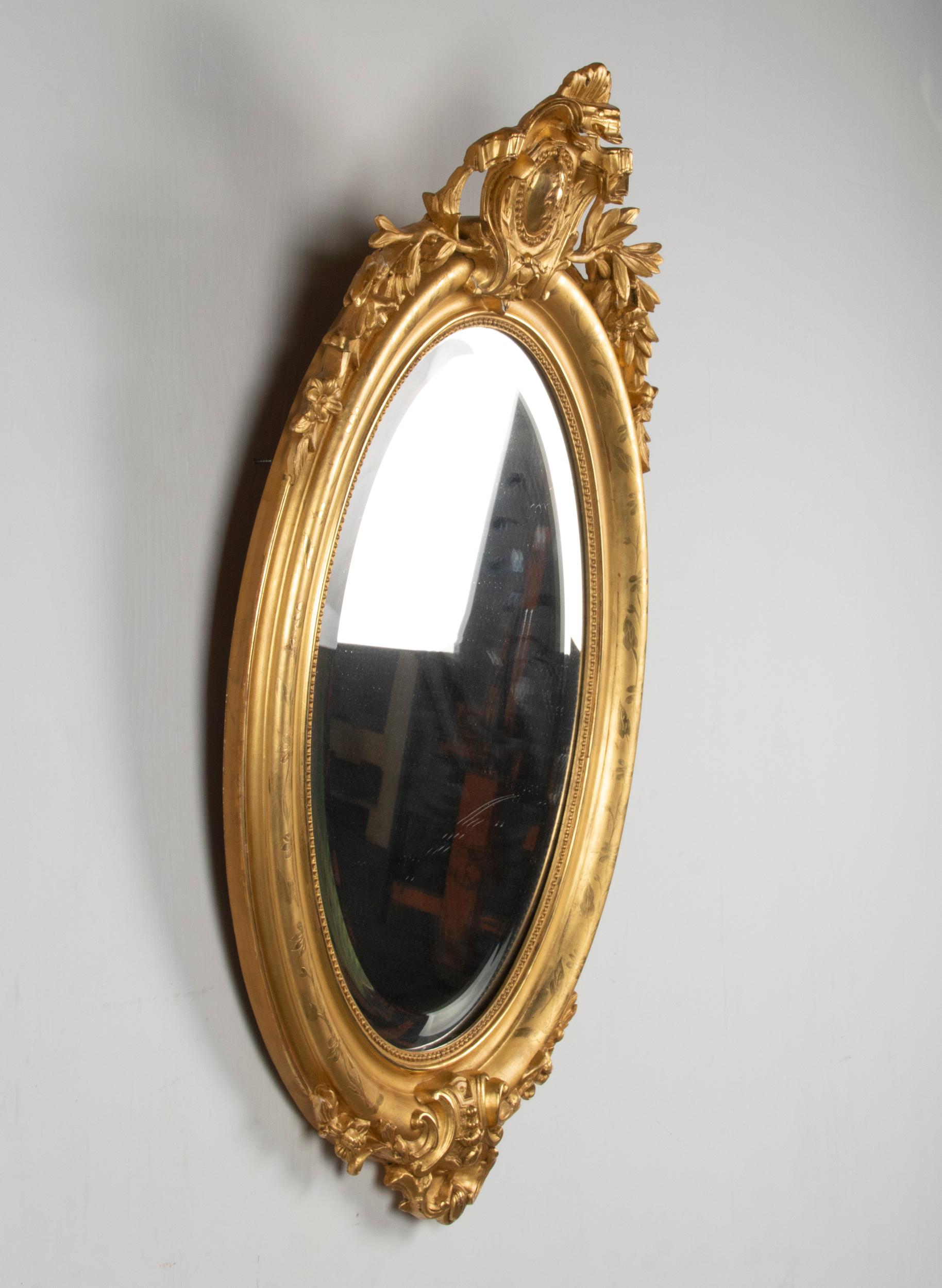 A 19th century Napoleon III period gilded oval mirror. Wooden hand carved crest with ribbons and laurel leaves, floral etched border. The gilding is in good condition with bright gilt. The beveled mirror glass facet is in good condition, without