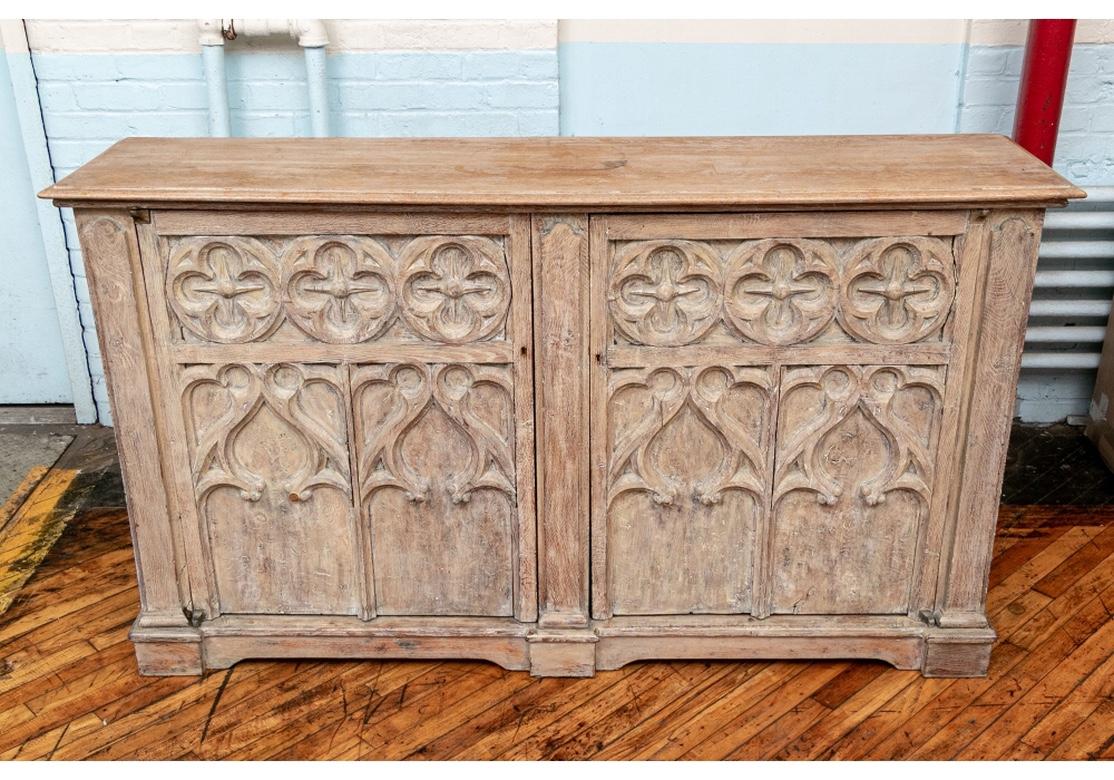 A large and impressive Neo-Gothic style cabinet, circa 1840. A heavy wide cabinet in a white wash with deeply carved double doors with Classic Gothic motifs of quatrefoils over arches. The keyholes with a key. The side supports with shaped tops and