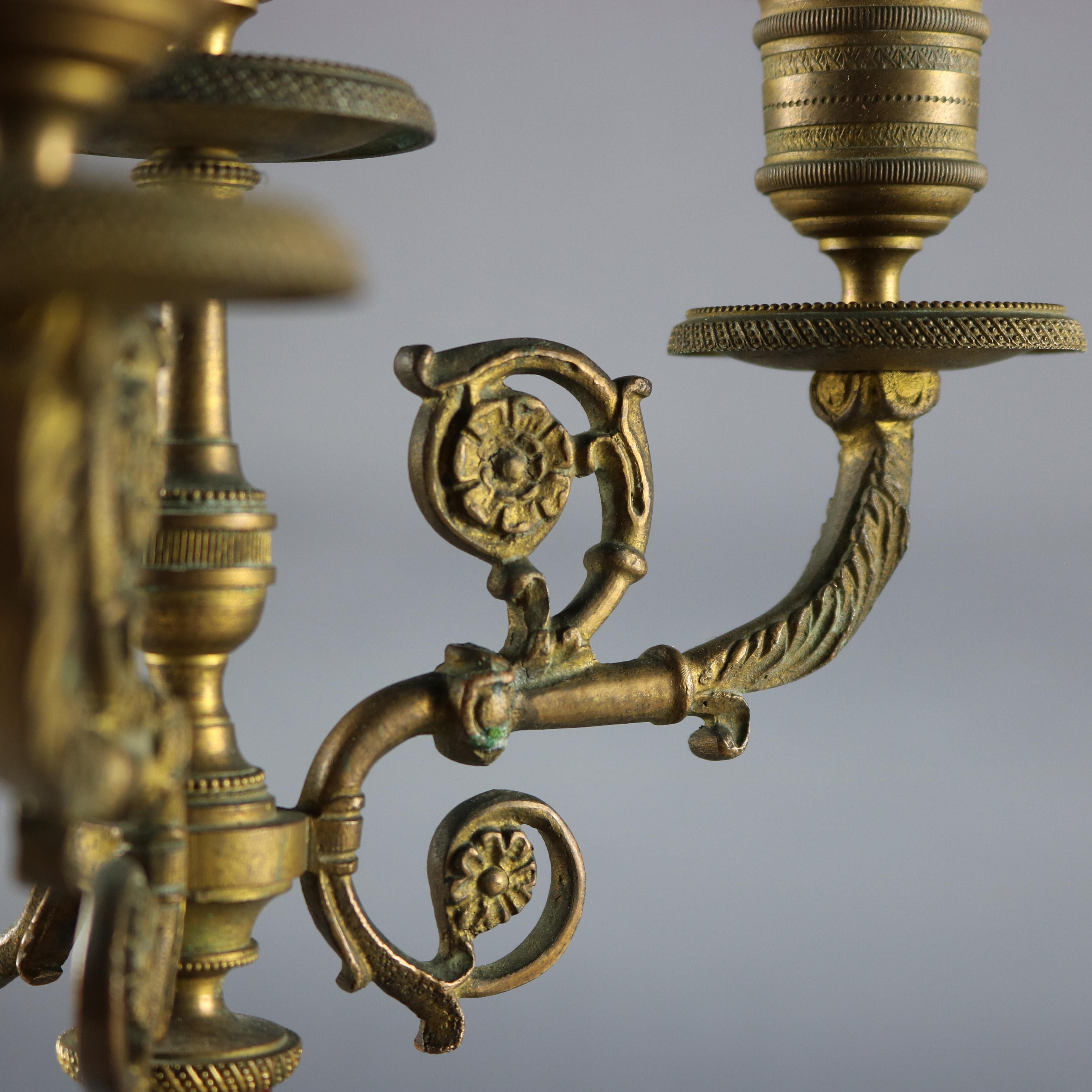 A pair of antique French Neoclassical candelabra feature three s-scroll and foliate cast bronze arms terminating in decorated candle sockets surrounding central candle surmounted on mahogany shaft raised on cast bronze tripod foliate decorated and