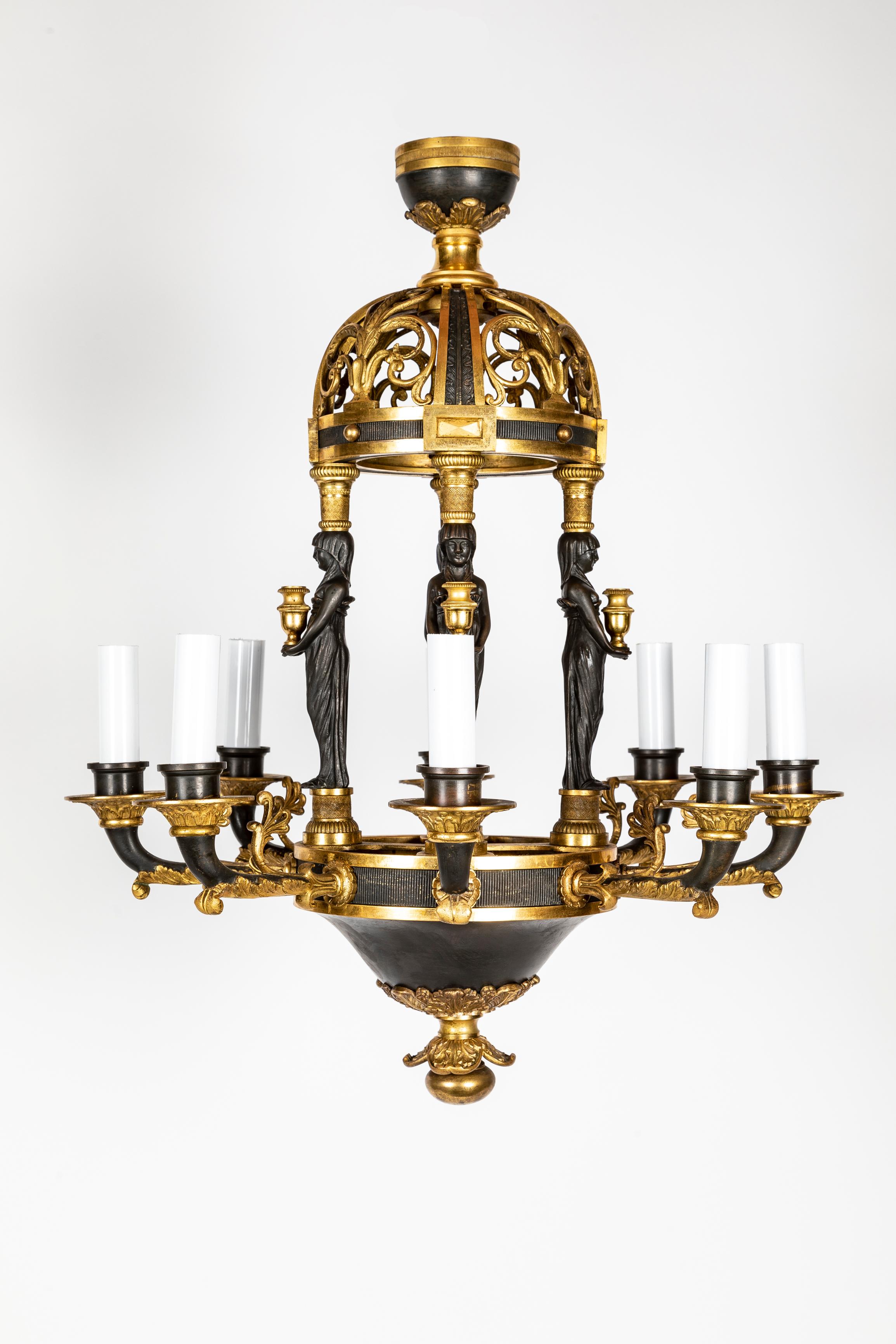 A Magnificent Antique French Empire Egyptian Revival gilt bronze and patinated bronze multi light chandelier of exquisite craftsmanship embellished with four patinated bronze neoclassical sculpted figures of women in draped gowns holding grecian