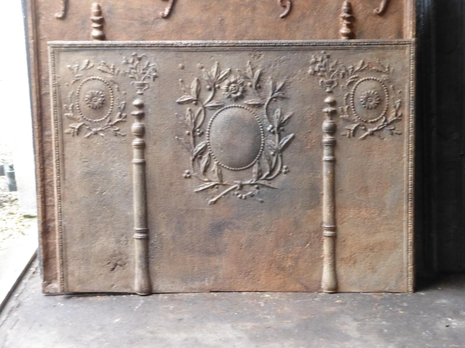 18th-19th century French neoclassical fireback with two pillars of Hercules. The pillars refer to the club of Hercules and stand for strength and the unknown. The pillars are topped with flower baskets. The laurel wreaths symbolize victory and