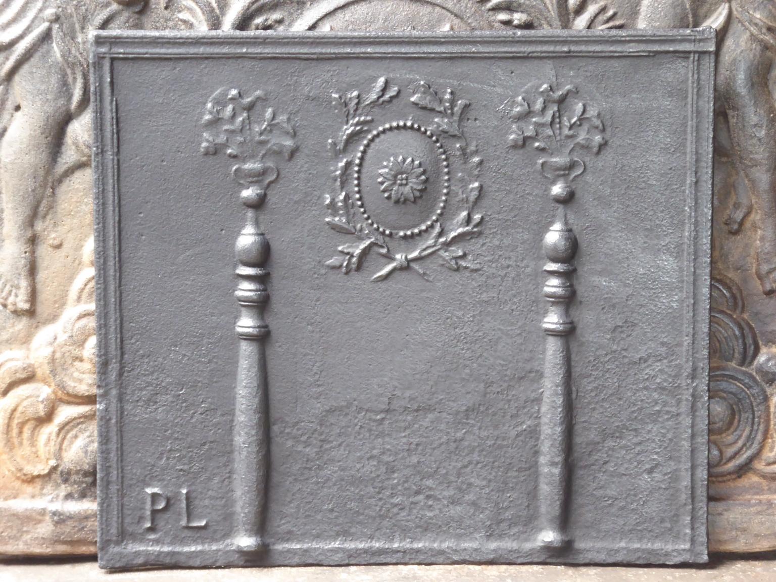 18th-19th century French neoclassical fireback with two pillars of Hercules. The pillars refer to the club of Hercules and stand for strength and the unknown. The pillars are topped with flower baskets. The laurel wreaths symbolize victory and