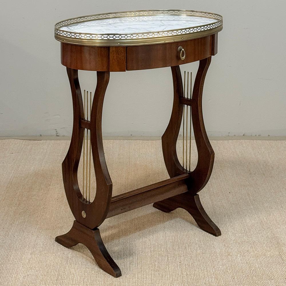 Antique French Neoclassical Oval End Table with Carrara Marble is a delightful design rendered to resemble a pair of lyres serving as side supports, with strings of brass!  The oval shaped top lends itself to a wide variety of seating group