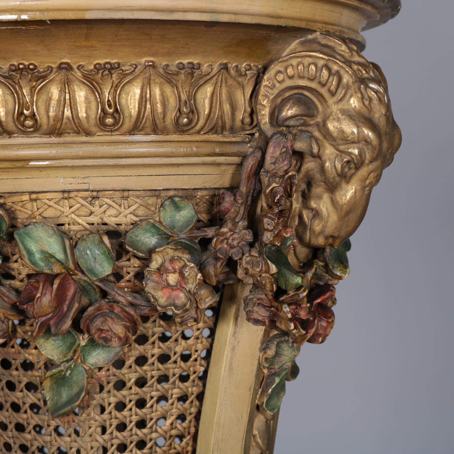 Antique French Neoclassical plant stand features giltwood frame with foliate collar having polychromed floral swags, beaded columns surmounted by rams heads support inverted cone form caned basket terminating in tiered acanthus and raised on foliate