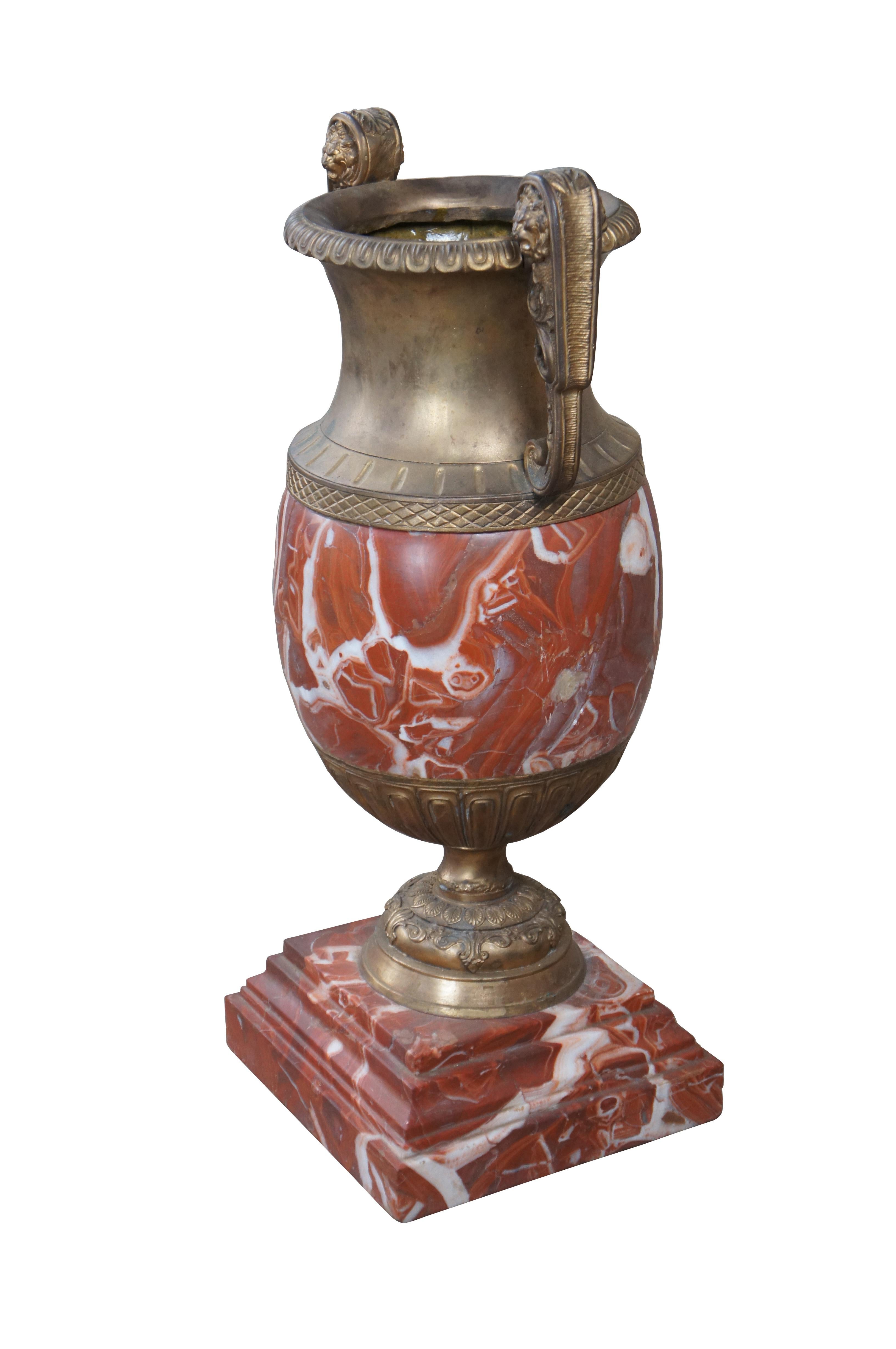 An eye catching late 19th century antique French rouge marble floor or mantel vase. Features a traditional urn shape with bronze mouth accented by ornate lion head mounted handles. Lower side of vase showcases gadrooning over an ornate foliate base.