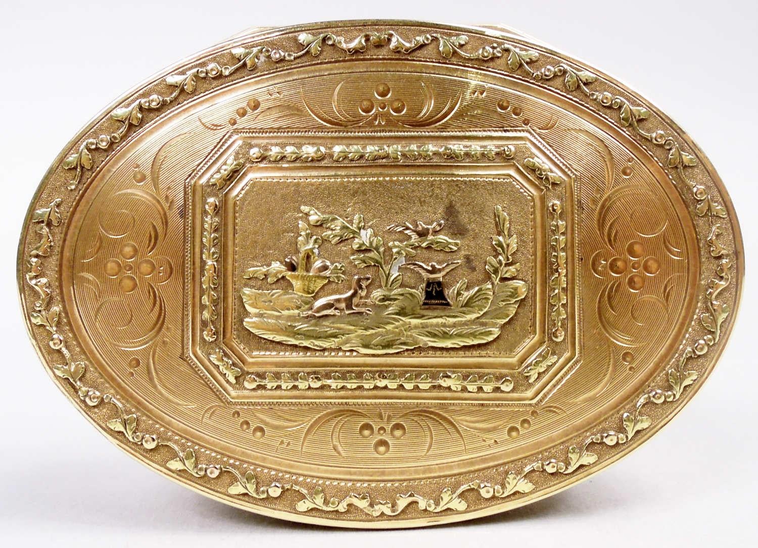 Tabatière néoclassique française en or 18 carats, vers 1800. Ovale avec des côtés droits ; couvercle à charnière. La partie supérieure de la couverture représente un jardin avec une végétation luxuriante et des paniers de fleurs habités par un chien