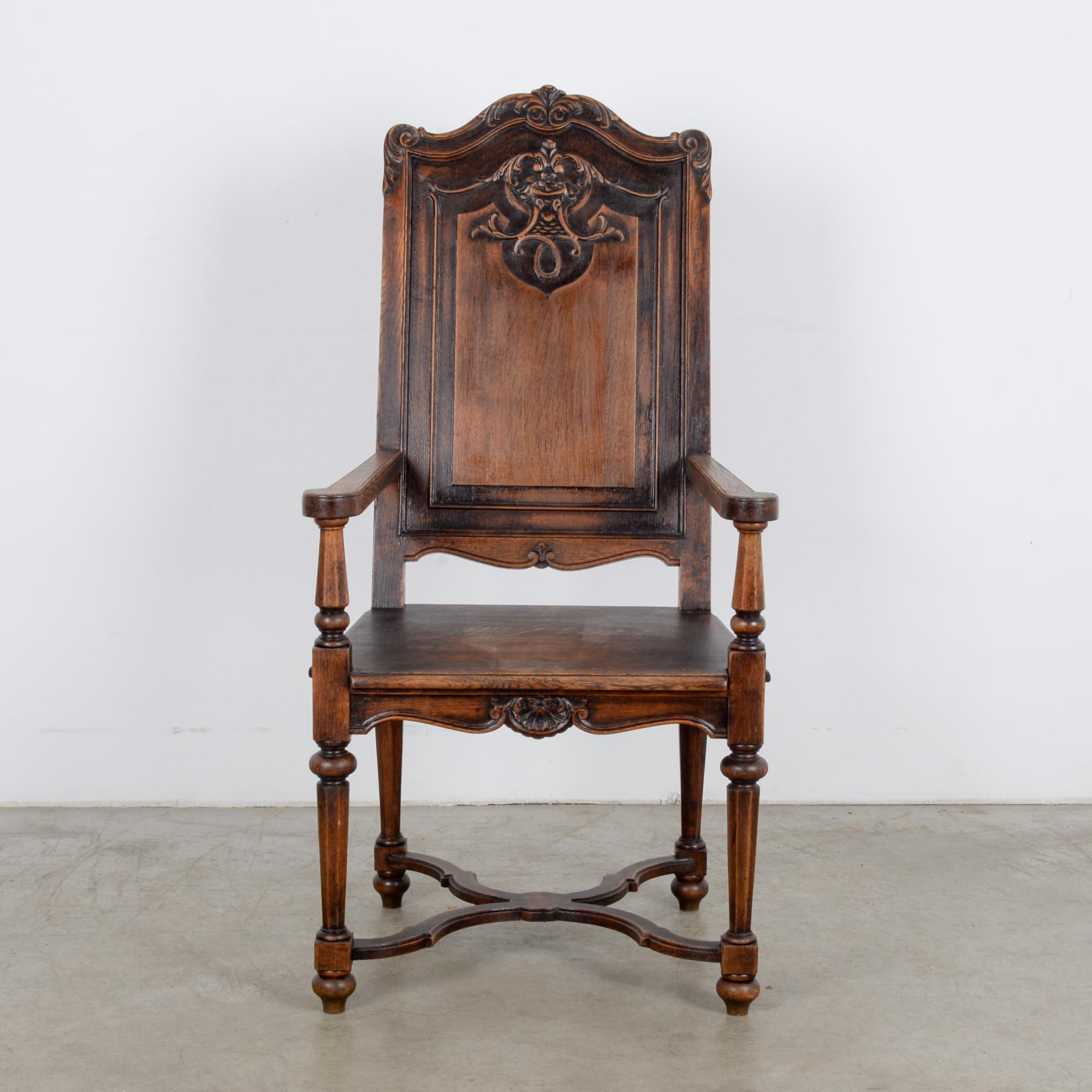 A wooden armchair from France, circa 1900. This seat is embellished with throne-like ornament, tapered legs connected by an undulating stretcher, scrolled apron with seashell relief, sloping stretching back carved with floral motif. This chair says