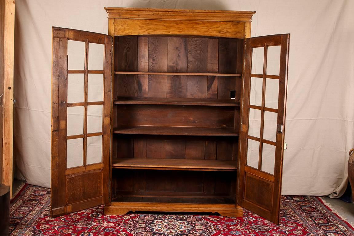 Antique French bookcase cabinet, oak double door cabinet with a carved cavetto cornice, eight glass windows on each door and recessed lower panels, bronze hardware with dolphin and animal heads at the top and bottom, the escutcheon with a key, four
