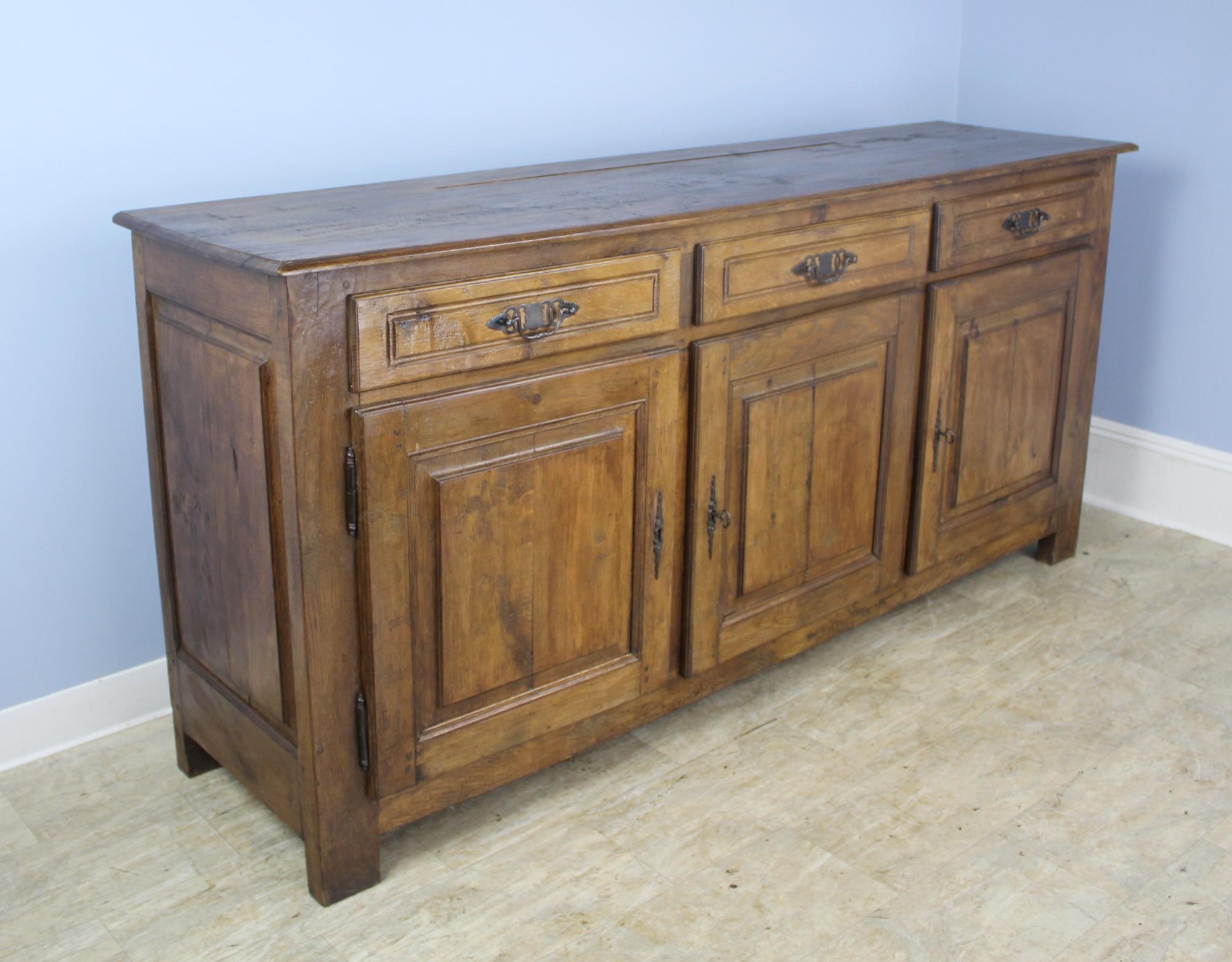 A handsome enfilade or three door French oak buffet with wonderful oak grain, color and patina. The carved panels on the doors and sides give this simple sturdy piece a note of good design interest. There is no separation between the two left doors,