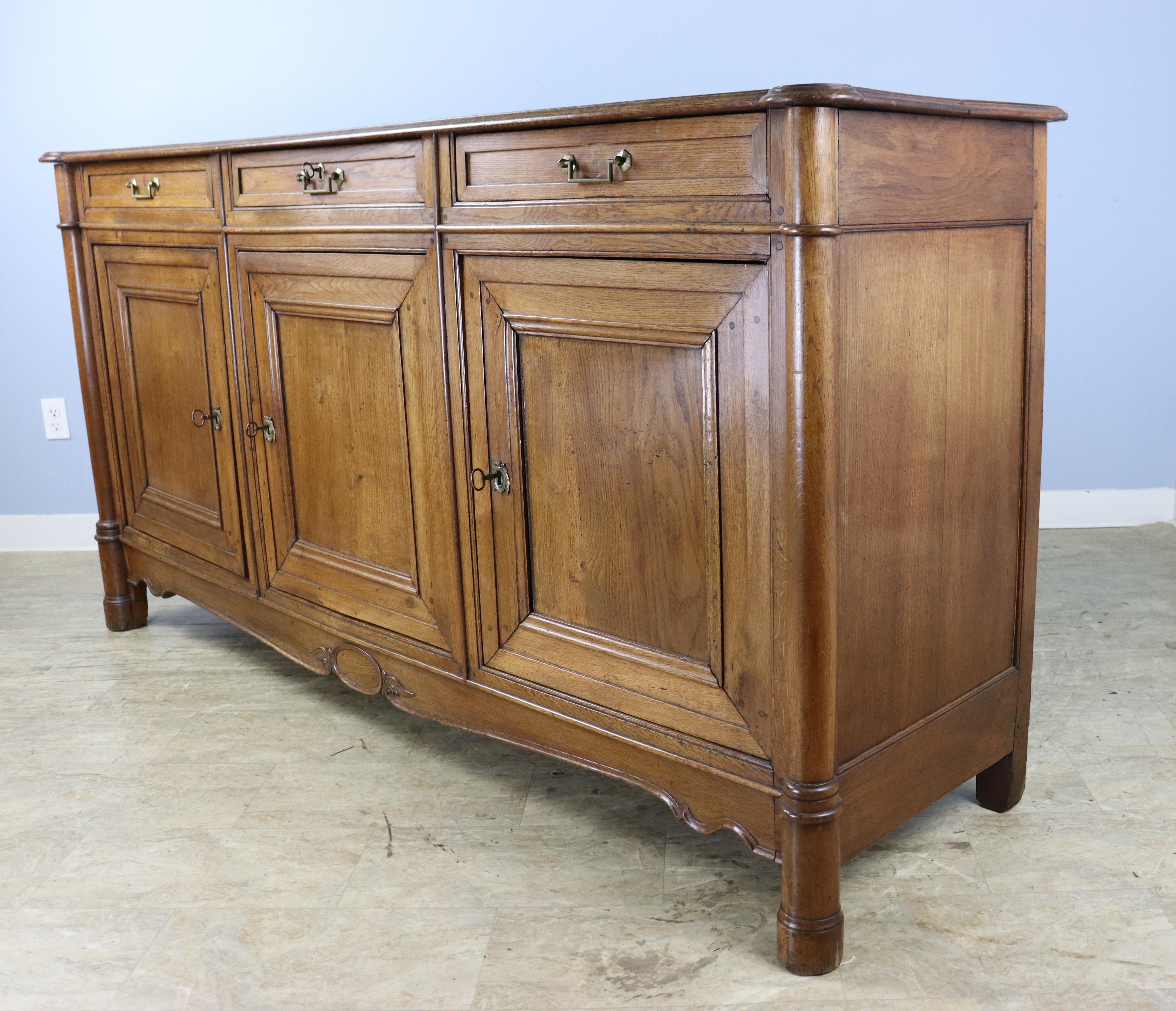 A handsome large three door oak buffet with wonderful oak color and soft patina.  The three doors open to a roomy single storage space.  Each door has its own key.  Elegant 3/4 column detail at the top corners and front feet and a whimsical carved