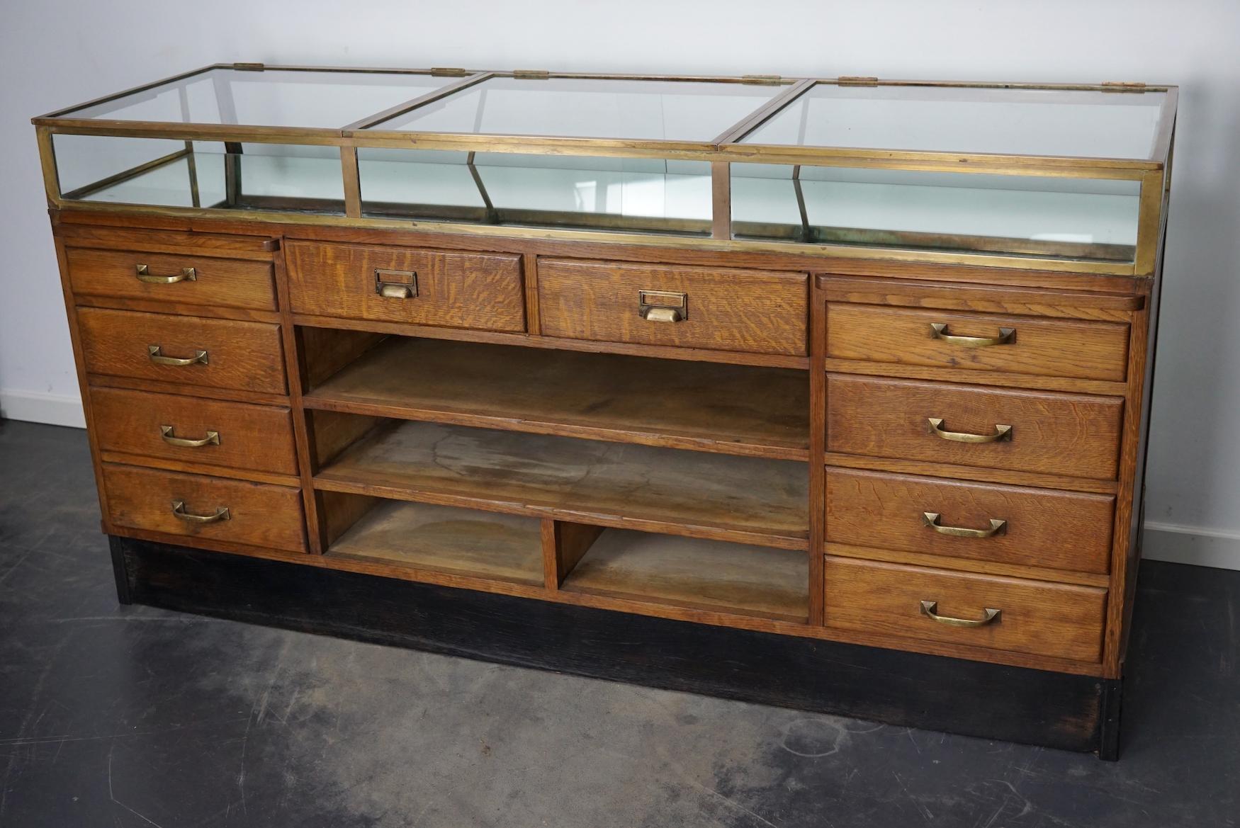 This vintage oak haberdashery shop counter dates from the 1920/30s and was made in France. It features a brass frame, glass doors / shelves and drawers in oak with brass handles. It was most likely used in a jewelry store.