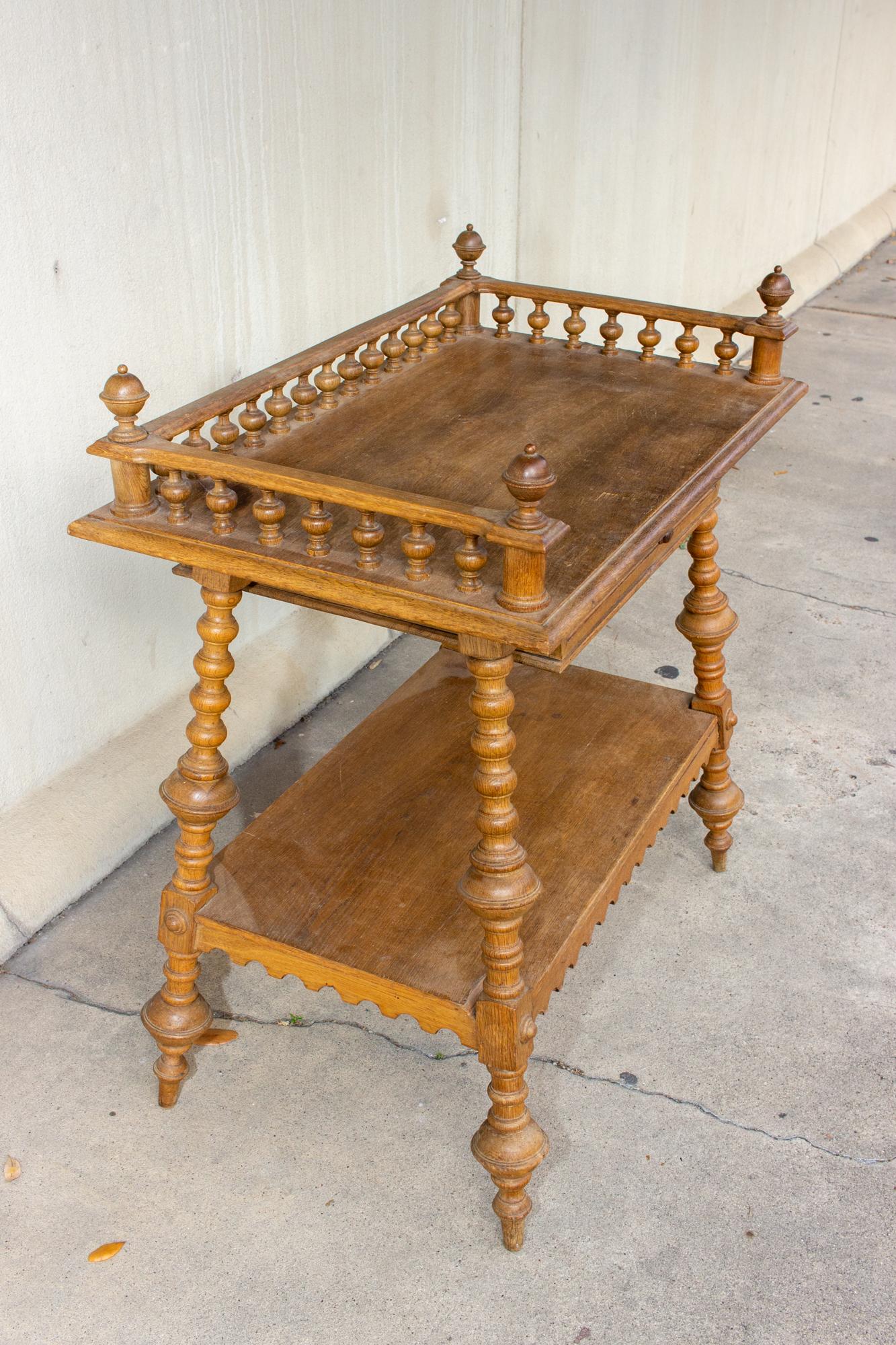 We envision this unique piece of antique French furniture as a bar table. The top tier has a gallery edge with ball-turned details and finials at each corner, and a drawer with dove-tail construction attached below. The lower shelf has a beautifully