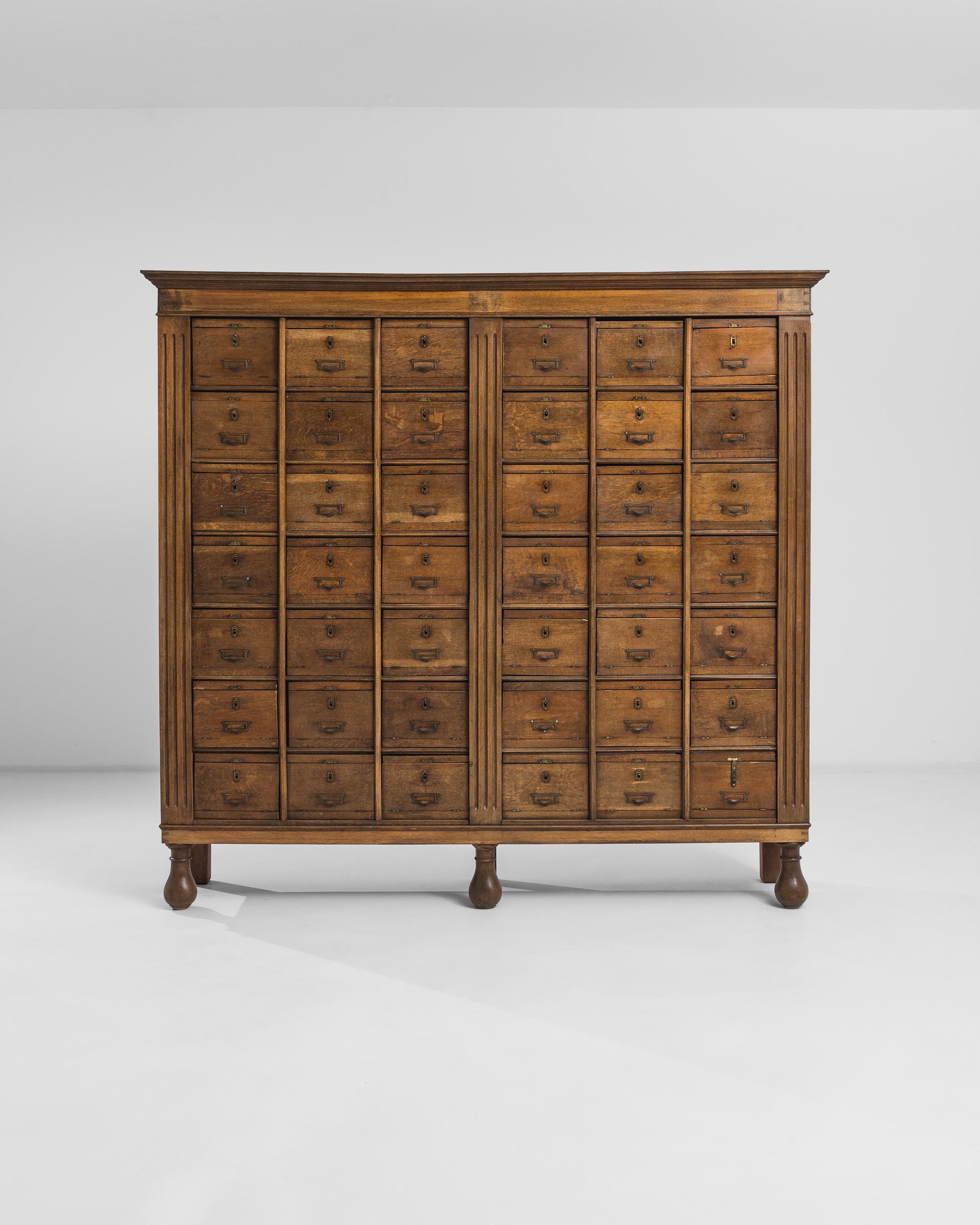 This antique cabinet was produced in France, circa 1900. A large wooden cabinet standing on bun feet, featuring a fluted case and an arrangement of forty-two drawers crowned by a beveled cornice. The piece flaunts a striking natural patina, offering