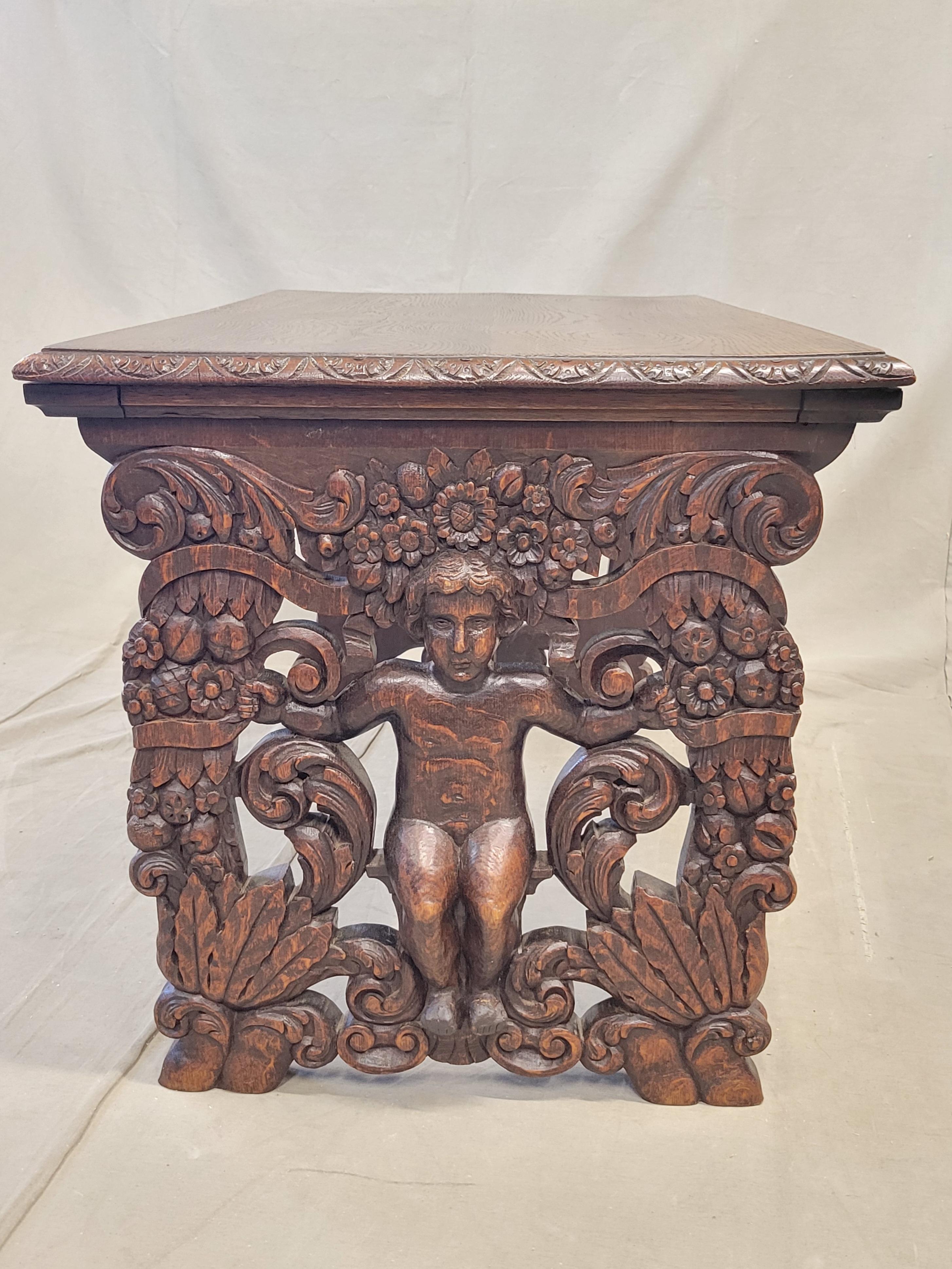 A unique antique French oak Renaissance Revival bench or coffee table with beautiful figural carvings surrounded by flowers and foliage on the legs. A stretcher with decorative carving spans the two legs. The top displays decorative carving around