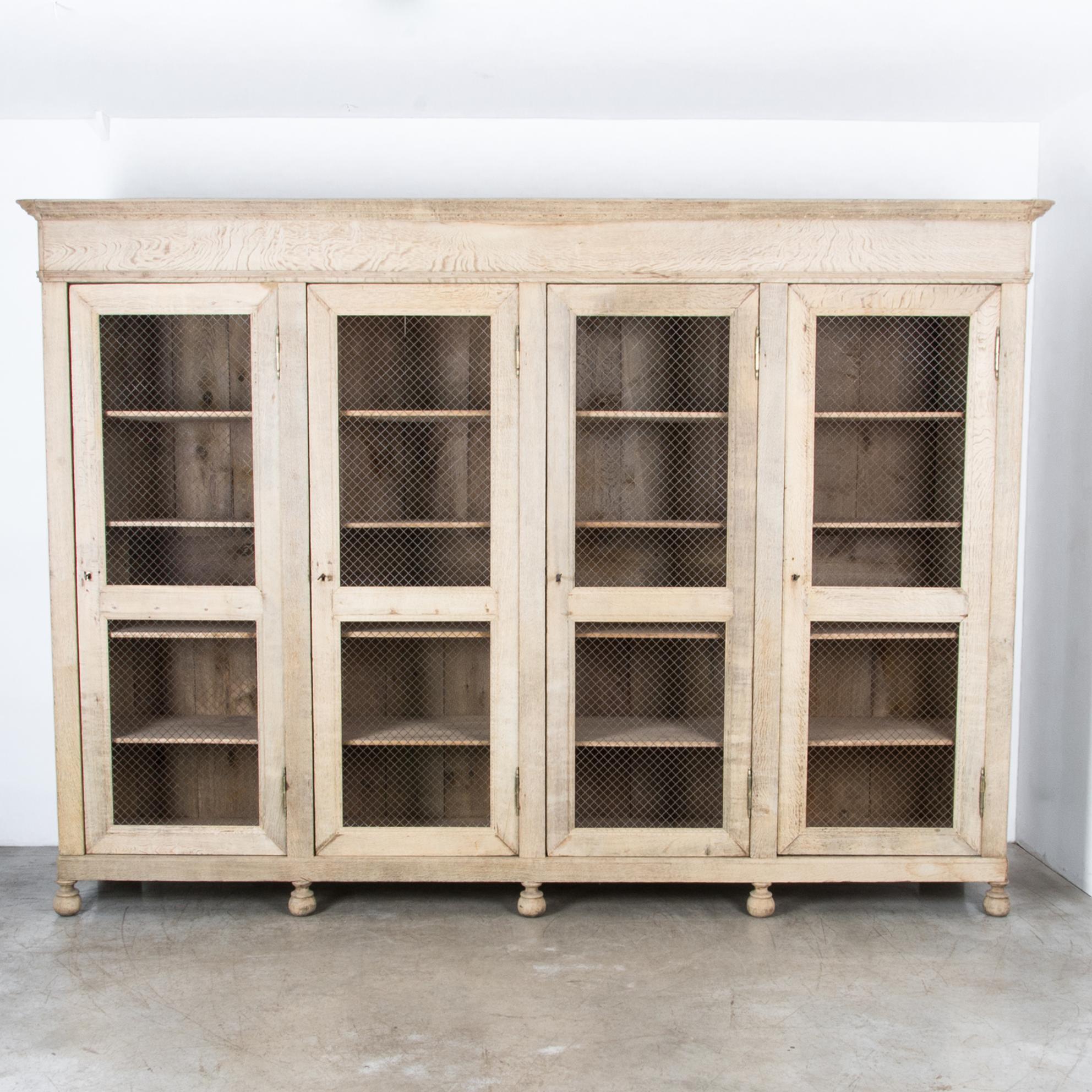 A distinctive storage piece from France, circa 1880. At nearly twelve feet, this four door cabinet is constructed in oak, with metal mesh screen doors. Resting on turned round feet, with a tall crown moulding, this piece features a distinctive mix