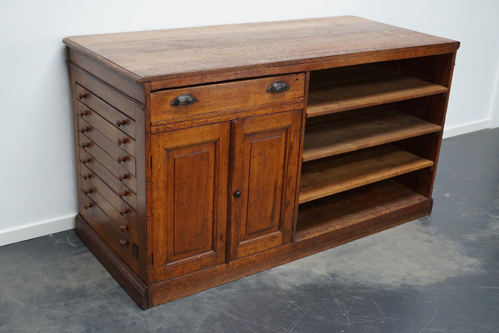 This antique oak shop counter dates from the turn of the century and was made in France. It features an oak paneled frame, shelves, drawers and two doors. Very unique item.