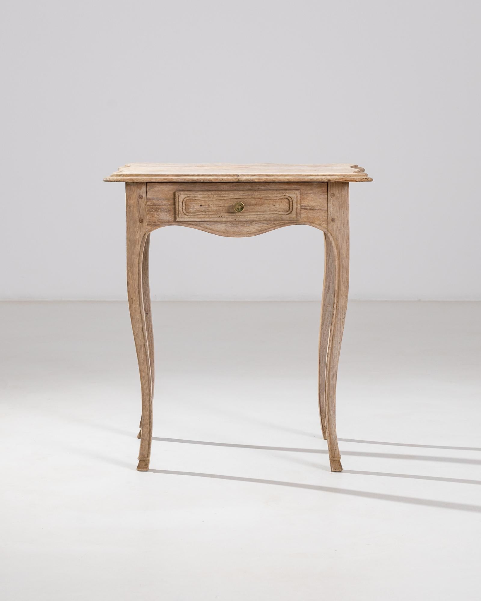 An antique bleached oak table from France with distinctive curved legs. Stylish and practical with a versatile shape, four limbs stretch to support the scalloped apron, set with a little drawer, and a softly beveled tabletop. 

Perched on cabriole