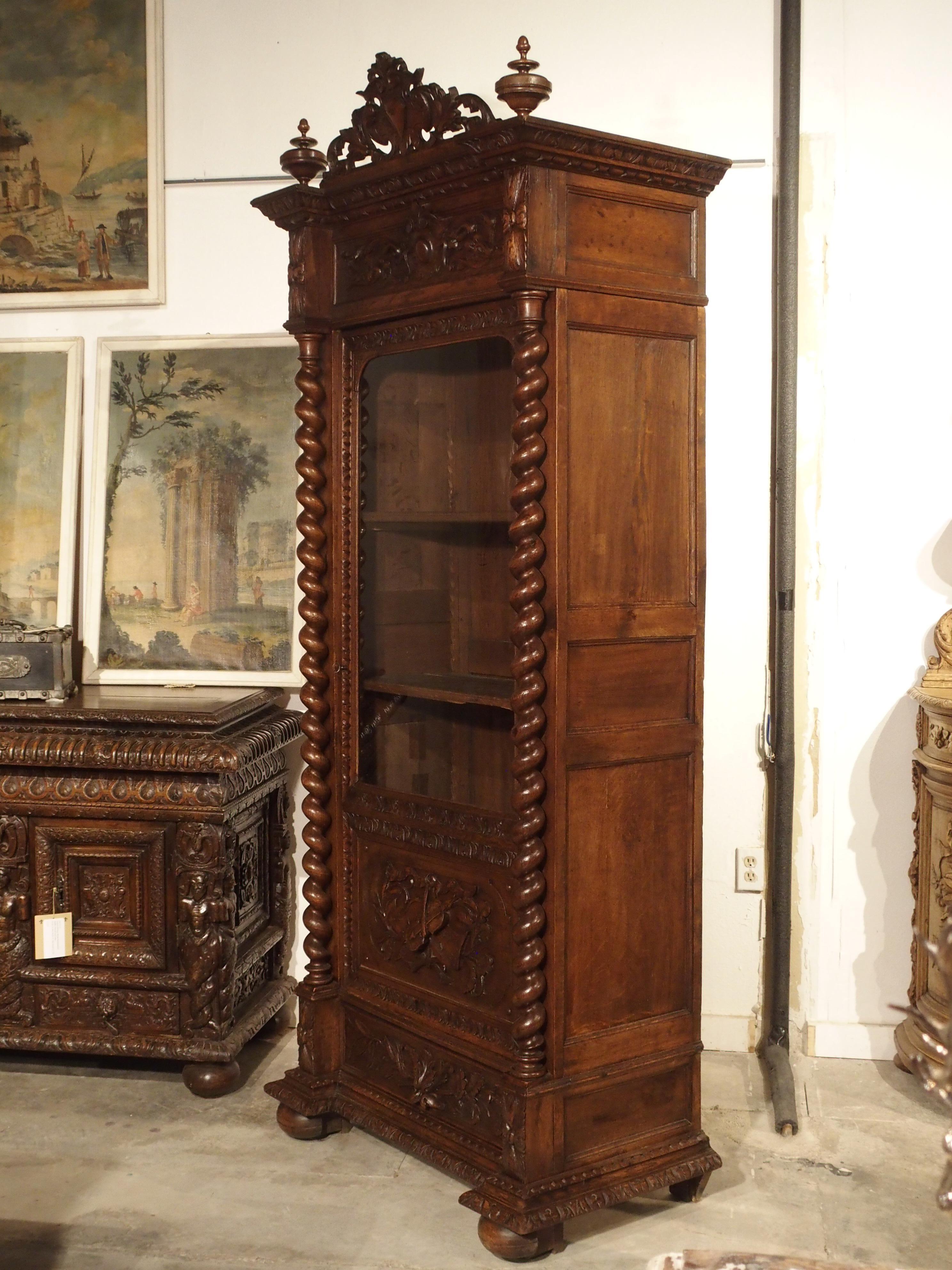 This handsome single door armoire, or display cabinet is known as a “vitrine” in France. It was made toward the end of the 1800s, constructed out of carved oak and hand blown glass. The lower door is decorated with a violin overlapping a scroll of