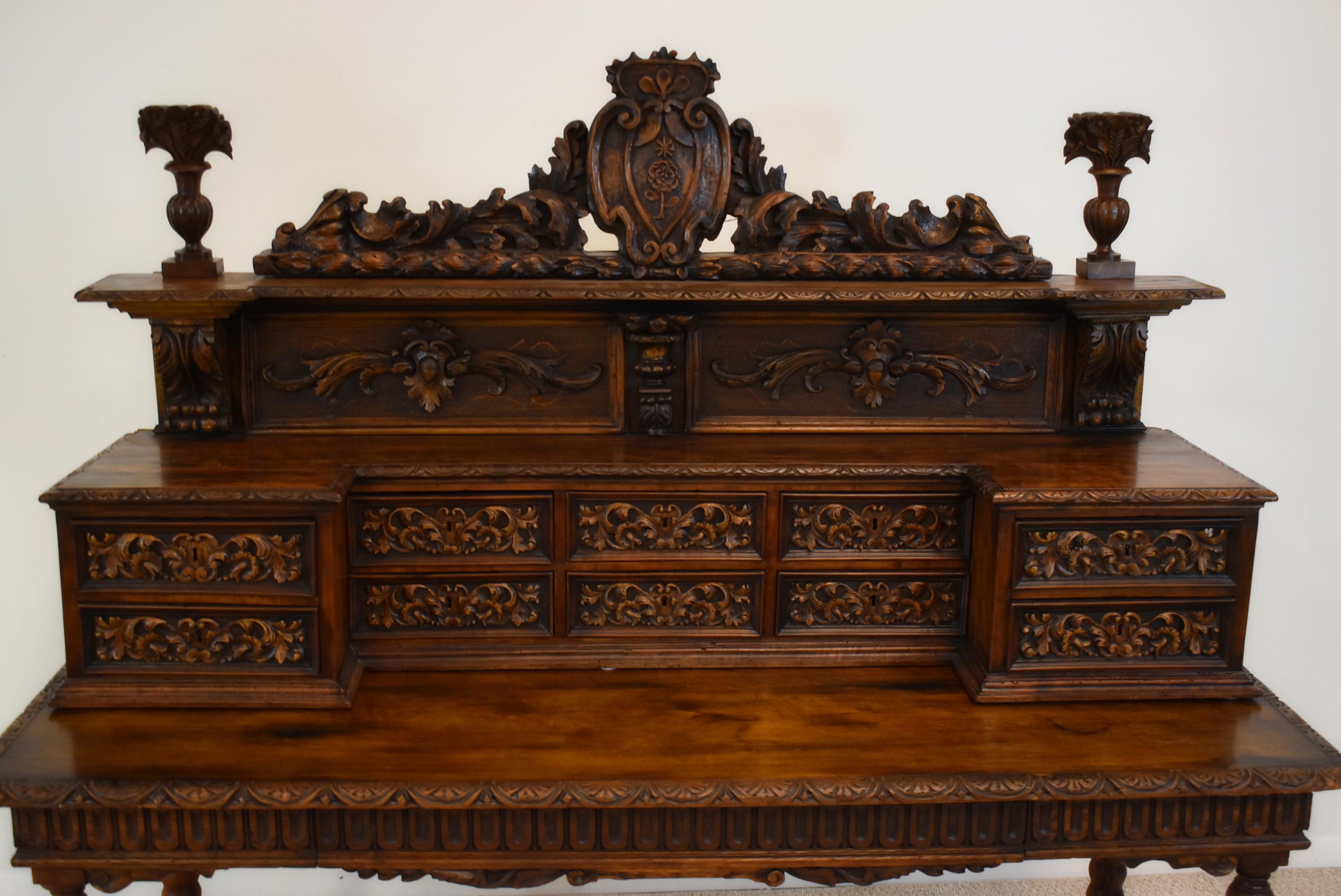 A late 19th century French two part writing desk. Oak construction with extensive hand carved detail, features a wall hanging upper section with scrolled crest and foliate detail above an open shelf and two tiers of five small drawers, separate base