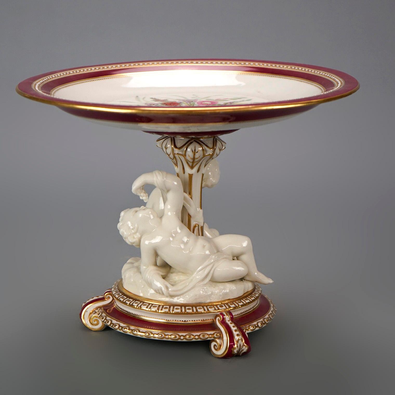 An antique French Old Paris figural compote offers porcelain construction with upper tray having hand painted floral decoration, raised on plinth with cherubs collecting grapes, raised on footed base, gilt highlights throughout, 19th