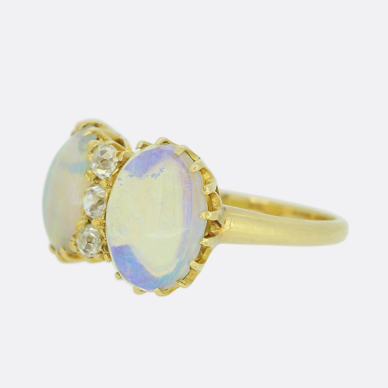 Here we have an antique French opal and diamond ring. This piece showcases two mesmerizing white cabochon opals showcasing eye capturing iridescent hues of blue, green, orange and pink. Nestled between the opals we find a trio round faceted old mine