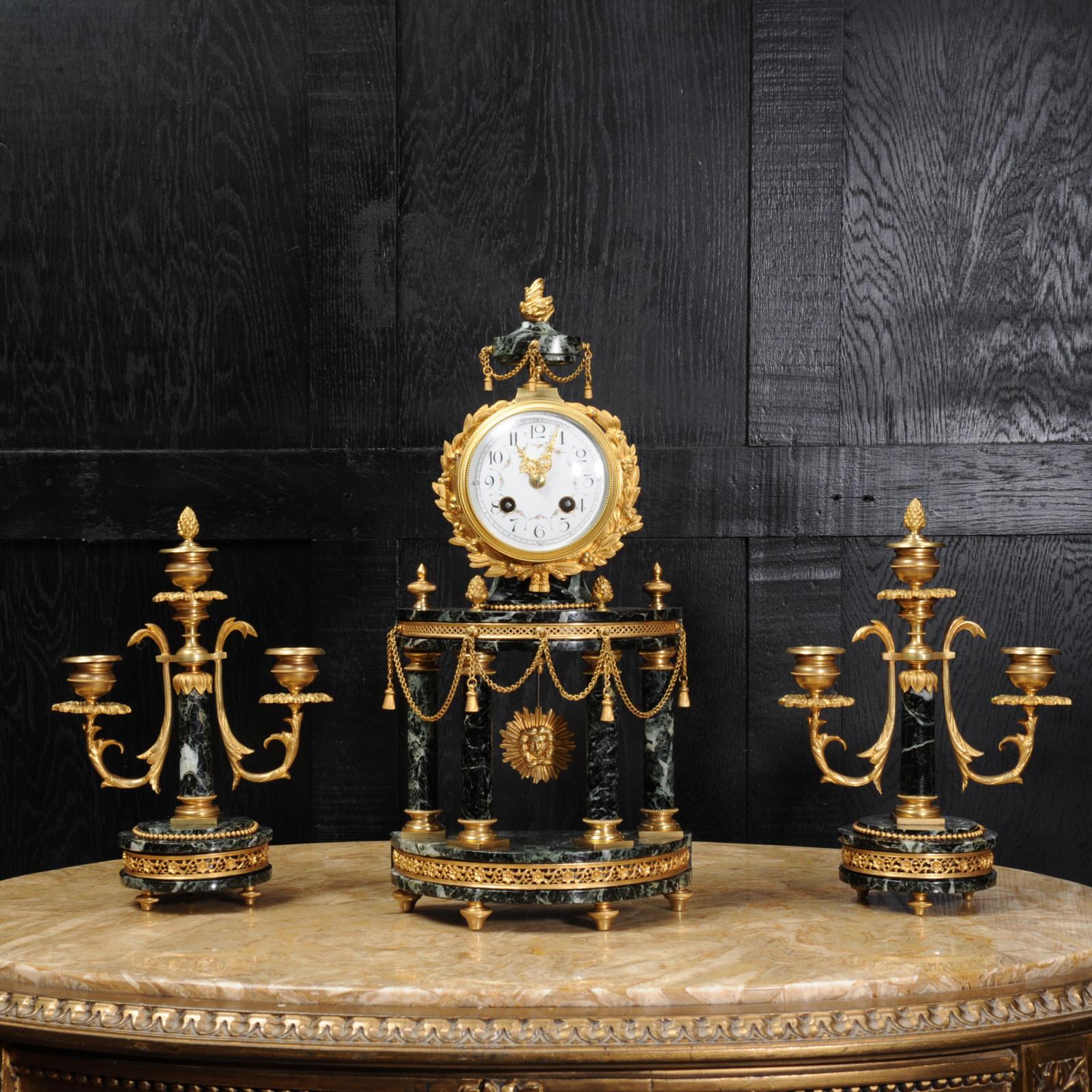 A superb original antique French clock set, circa 1900, beautifully modelled in a stunning variegated green marble with gilded bronze mounts. The clock is formed as a four pillar portico, the movement mounted in a drum with the ormolu pendulum